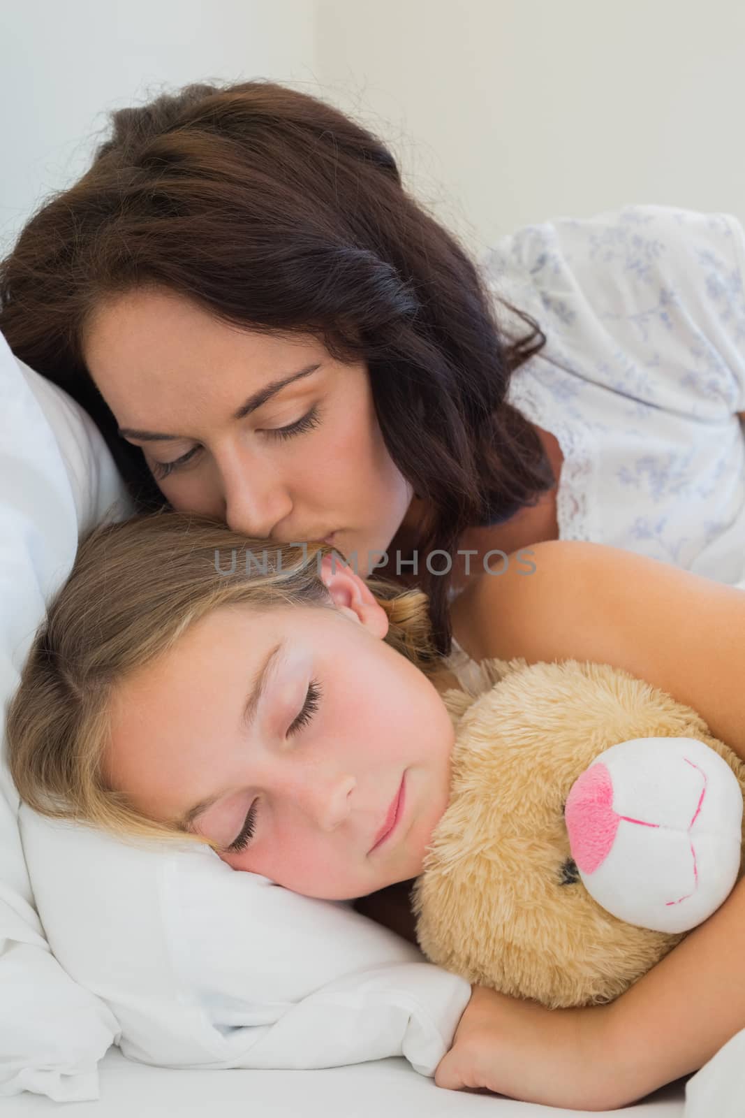 Beautiful mother kissing sleeping daughter in bed at home