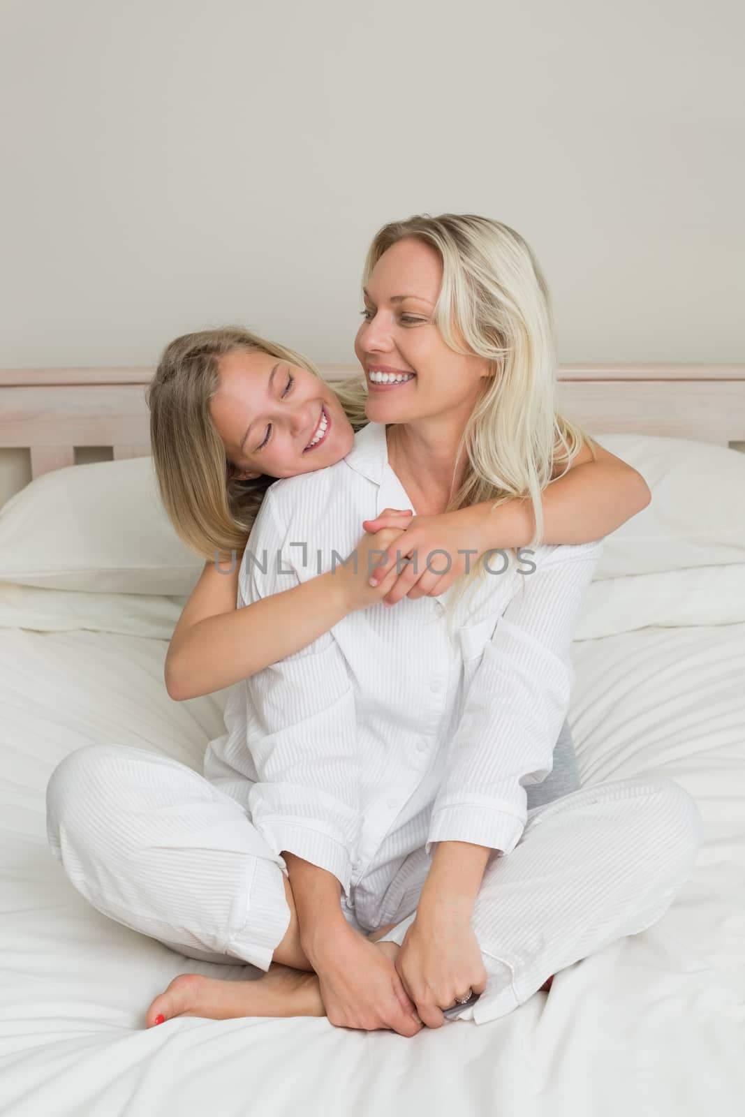 Girl embracing mother sitting in bed  by Wavebreakmedia