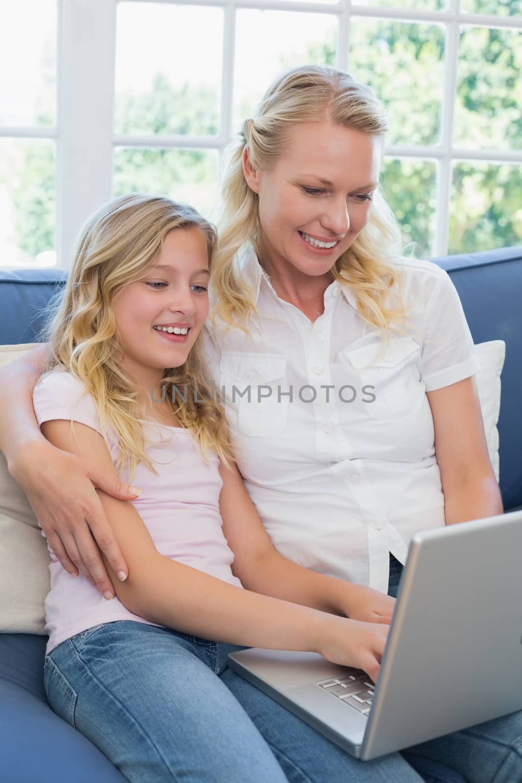 Happy mother and daughter using laptop together on sofa at home