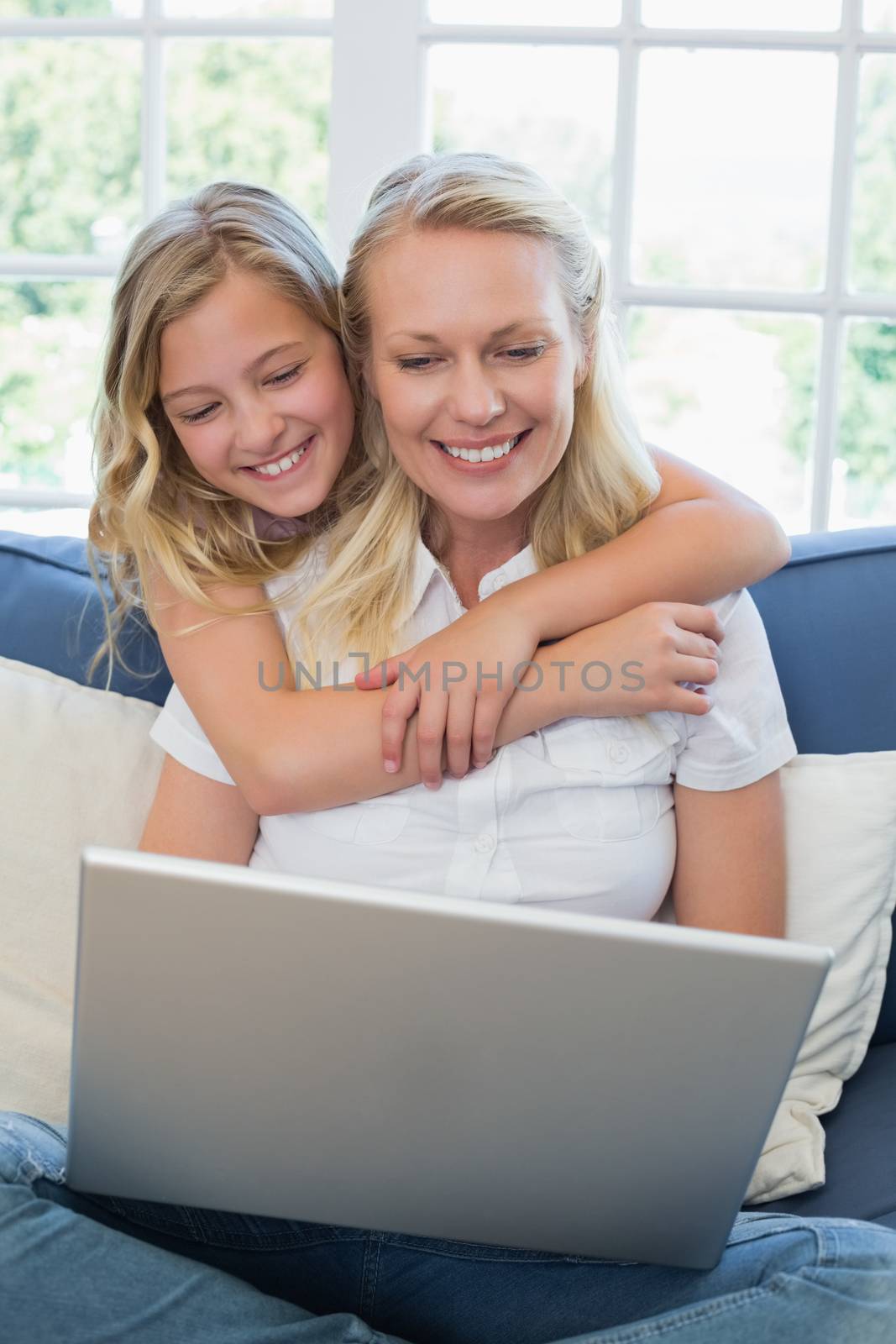 Cute girl embracing mother using laptop in house