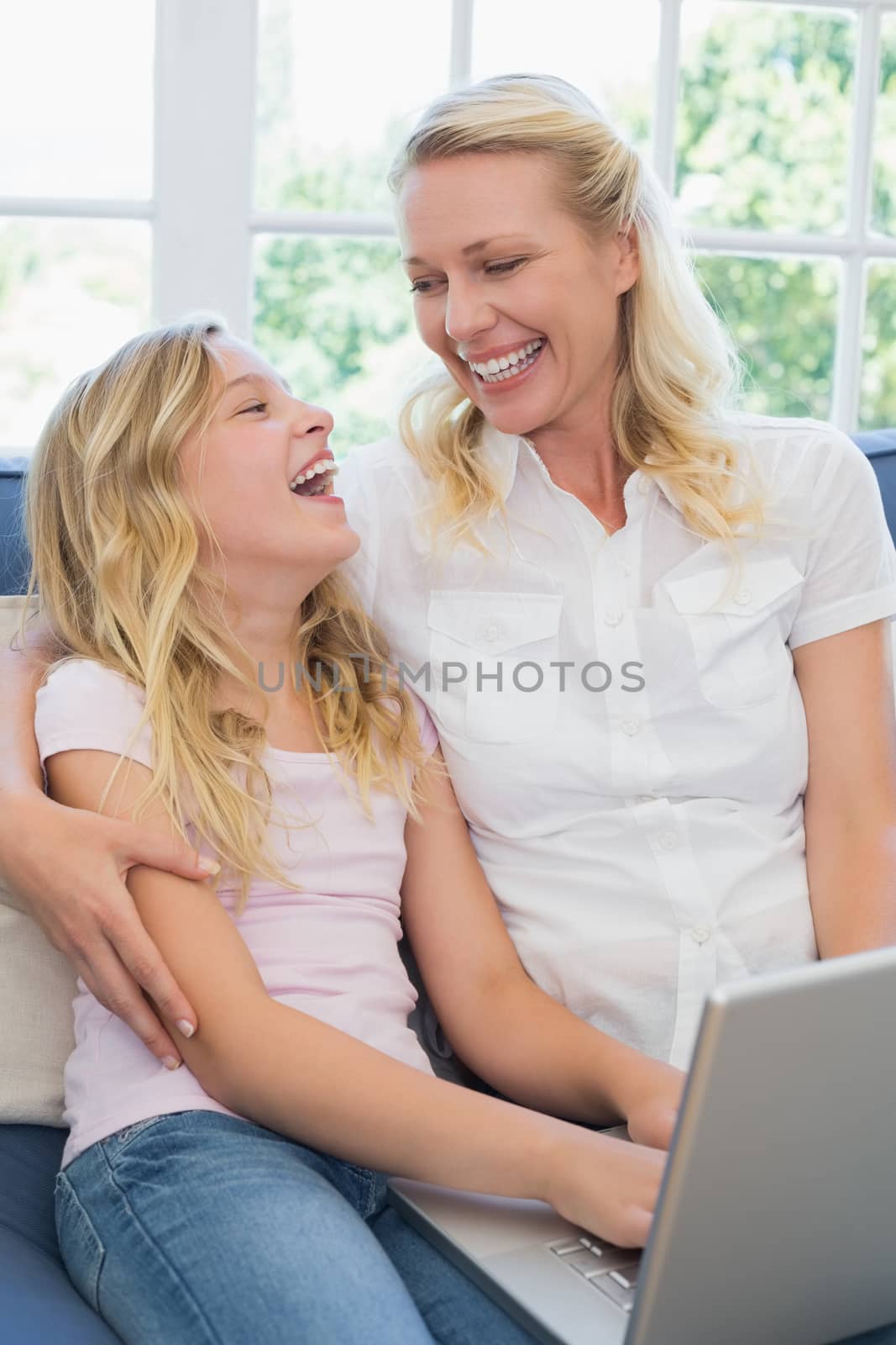 Happy mother and daughter looking at each other while using laptop on sofa at home