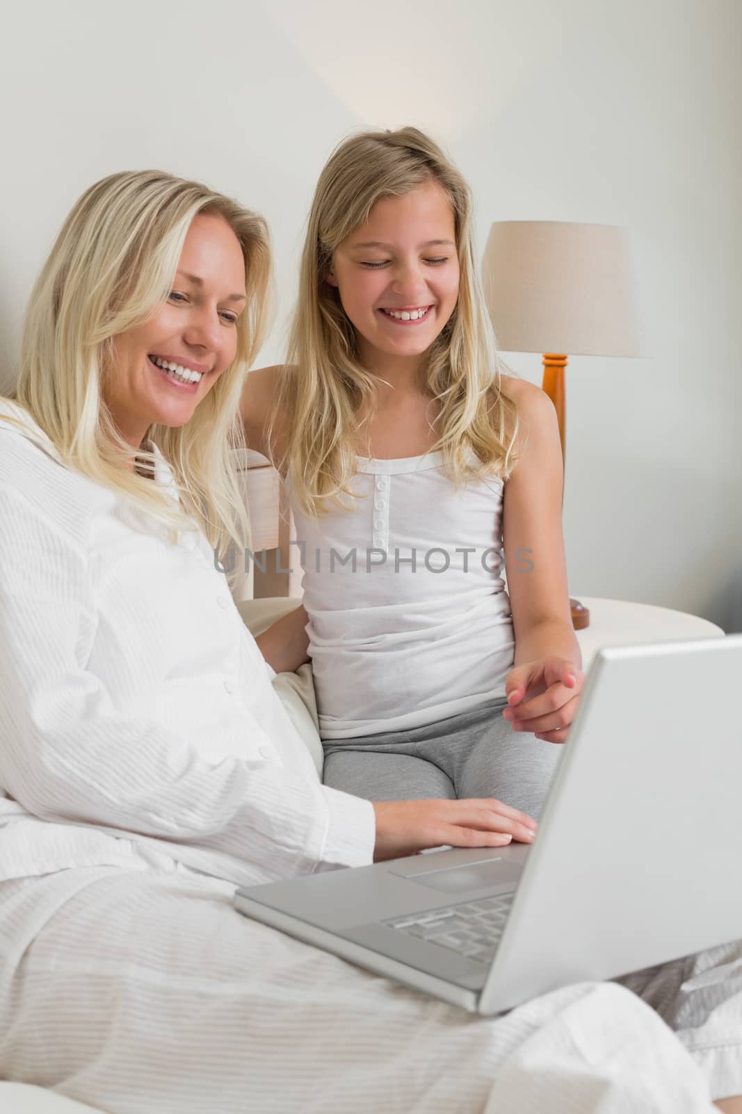 Cheerful mother and daughter using laptop in bed by Wavebreakmedia
