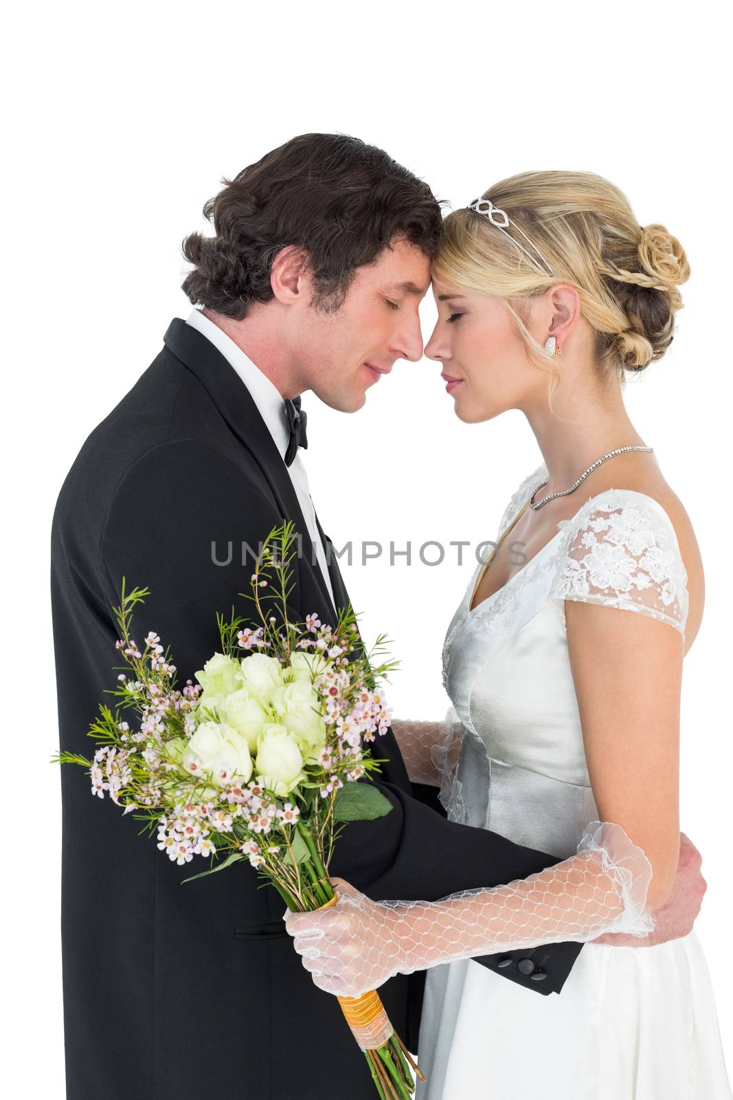 Side view of romantic newlywed couple standing head to head on white background