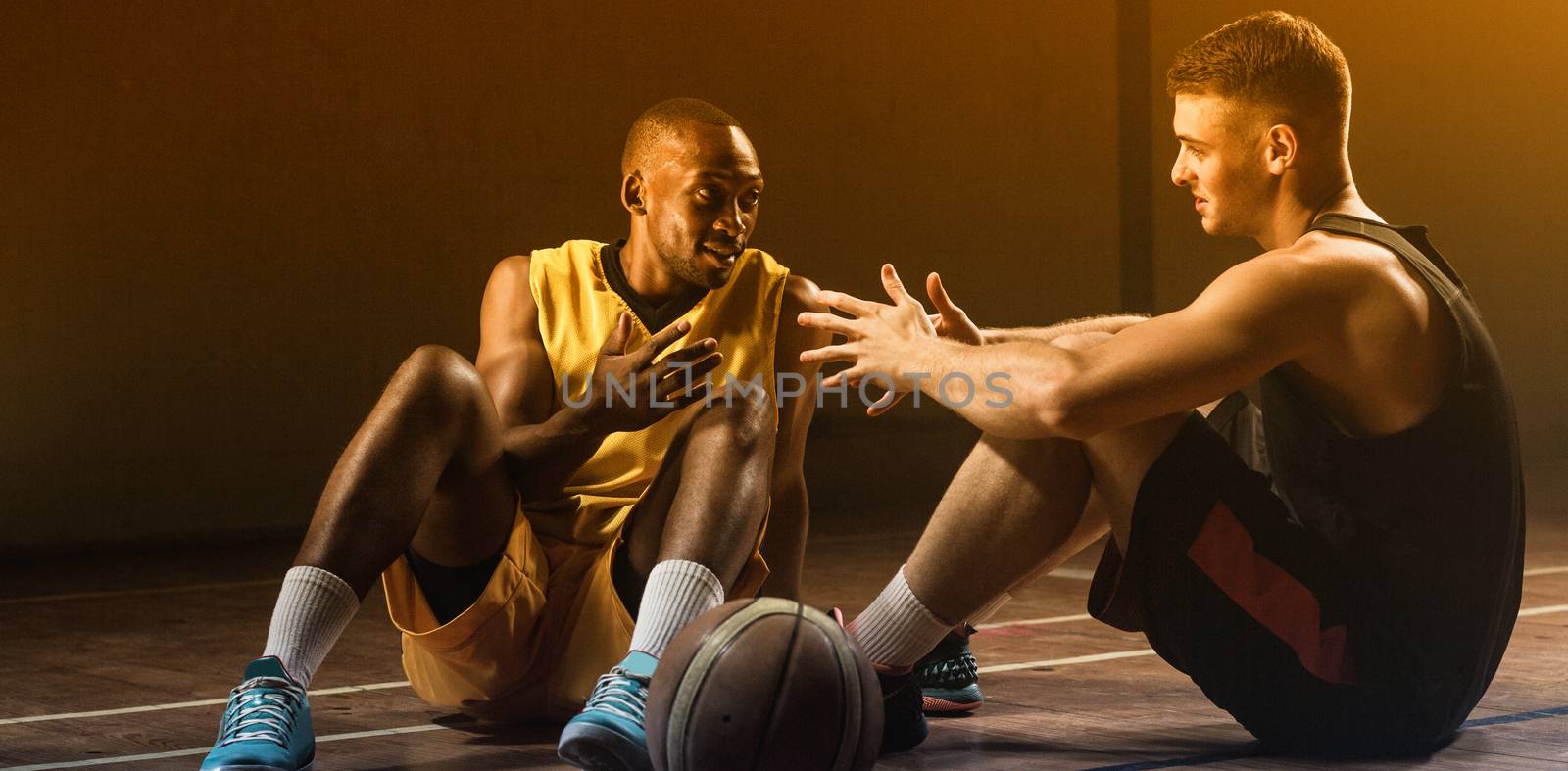 Basketball players sitting on floor talking together on gym 