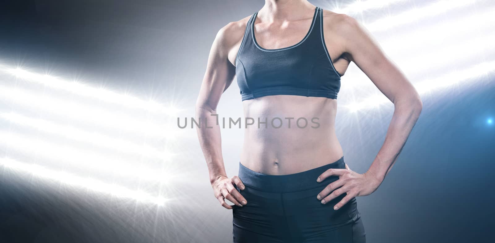 Female athlete standing with hand on hip against spotlights