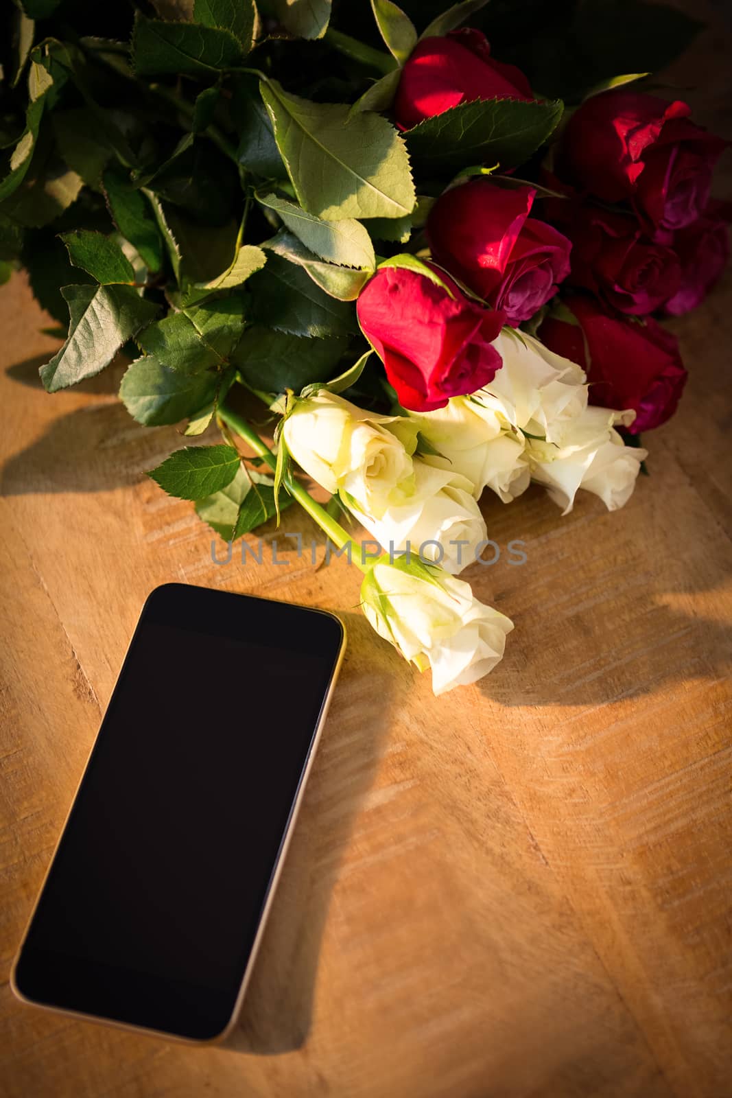 Close-up of yellow and red roses with smartphone on the wooden table