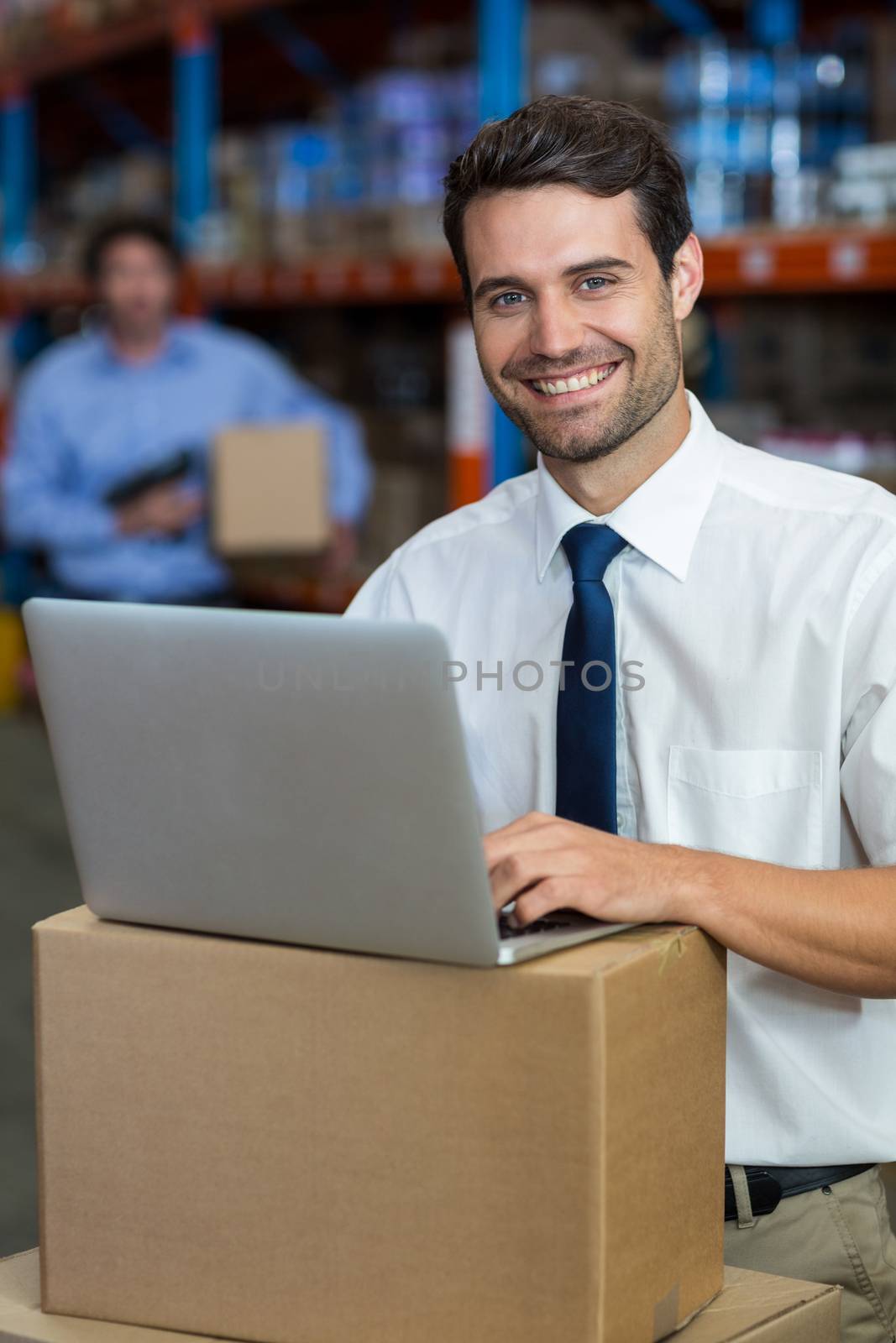 Portrait of happy manager using a laptop put on cardboard in a warehouse