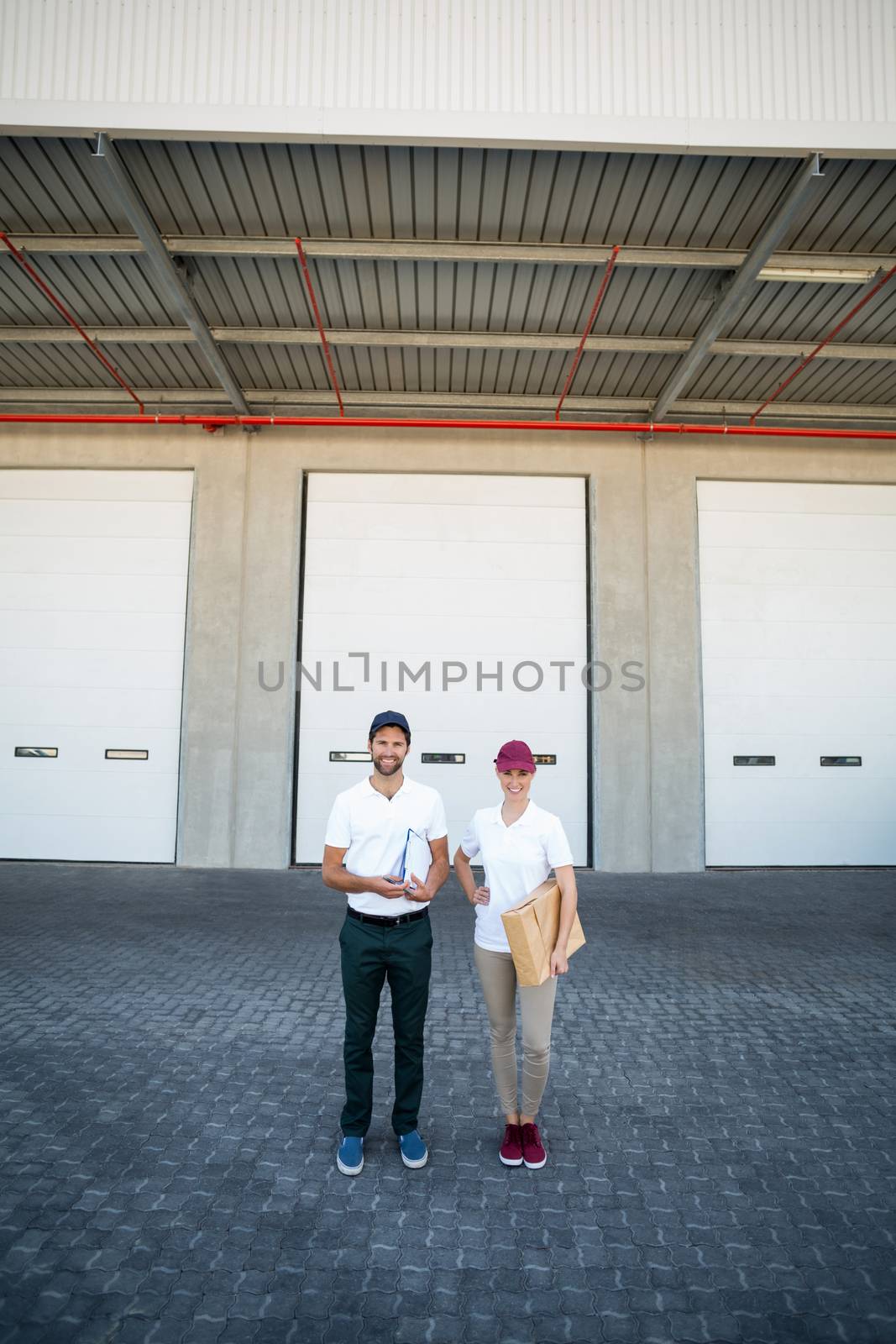 Delivery people are posing and holding goods in front of a warehouse