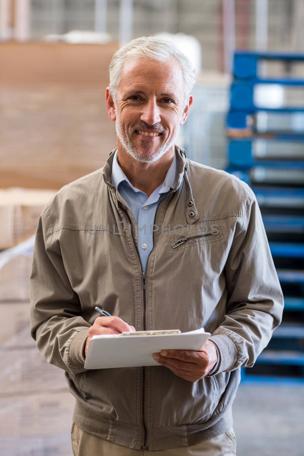 Portrait of manager is holding a clipboard and smiling to the camera in a warehouse