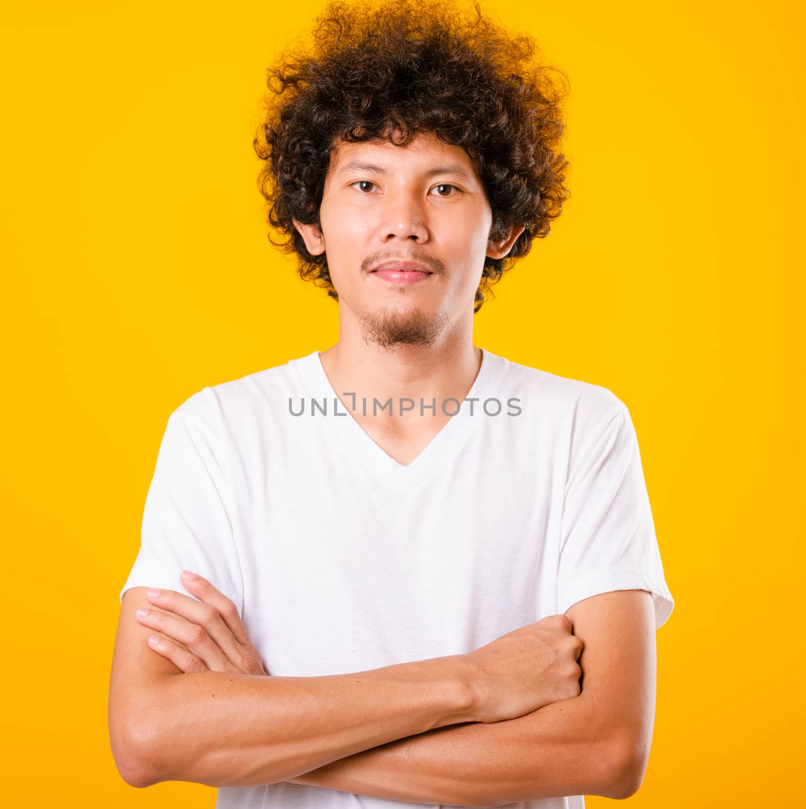 Portrait of Asian handsome man with curly hair with arms crossed isolate on yellow background