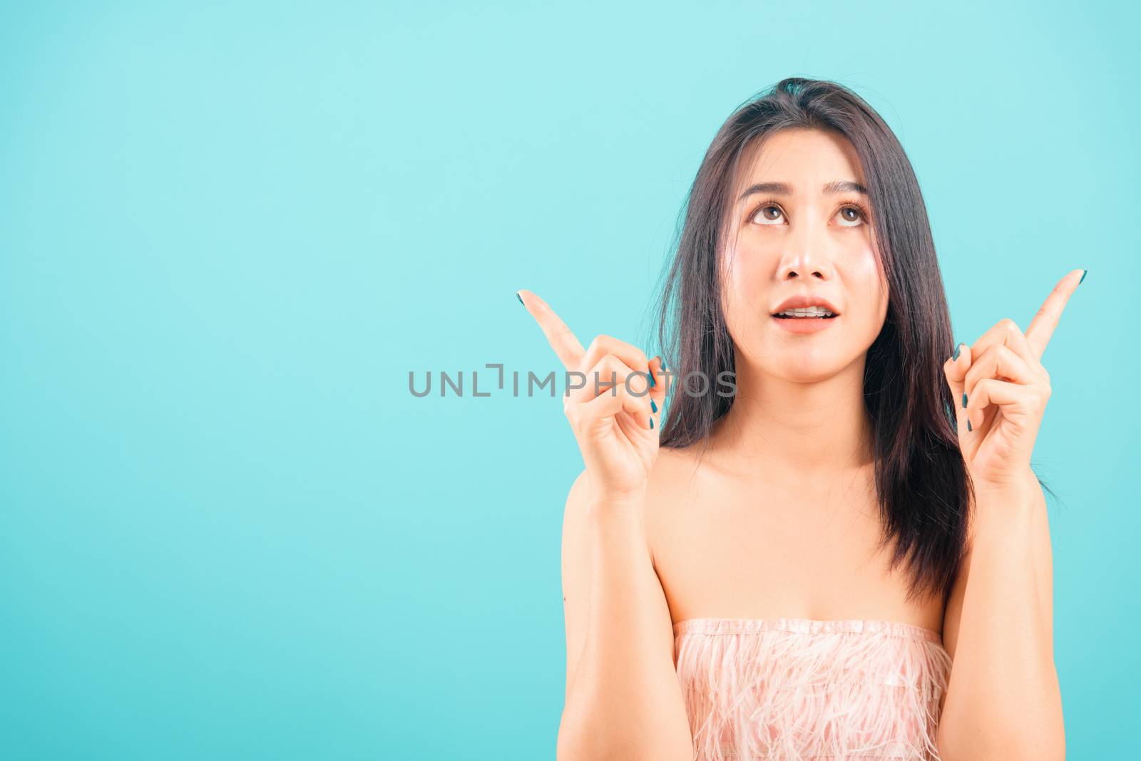 Smiling face Asian beautiful woman her point up on blue background, with copy space for text