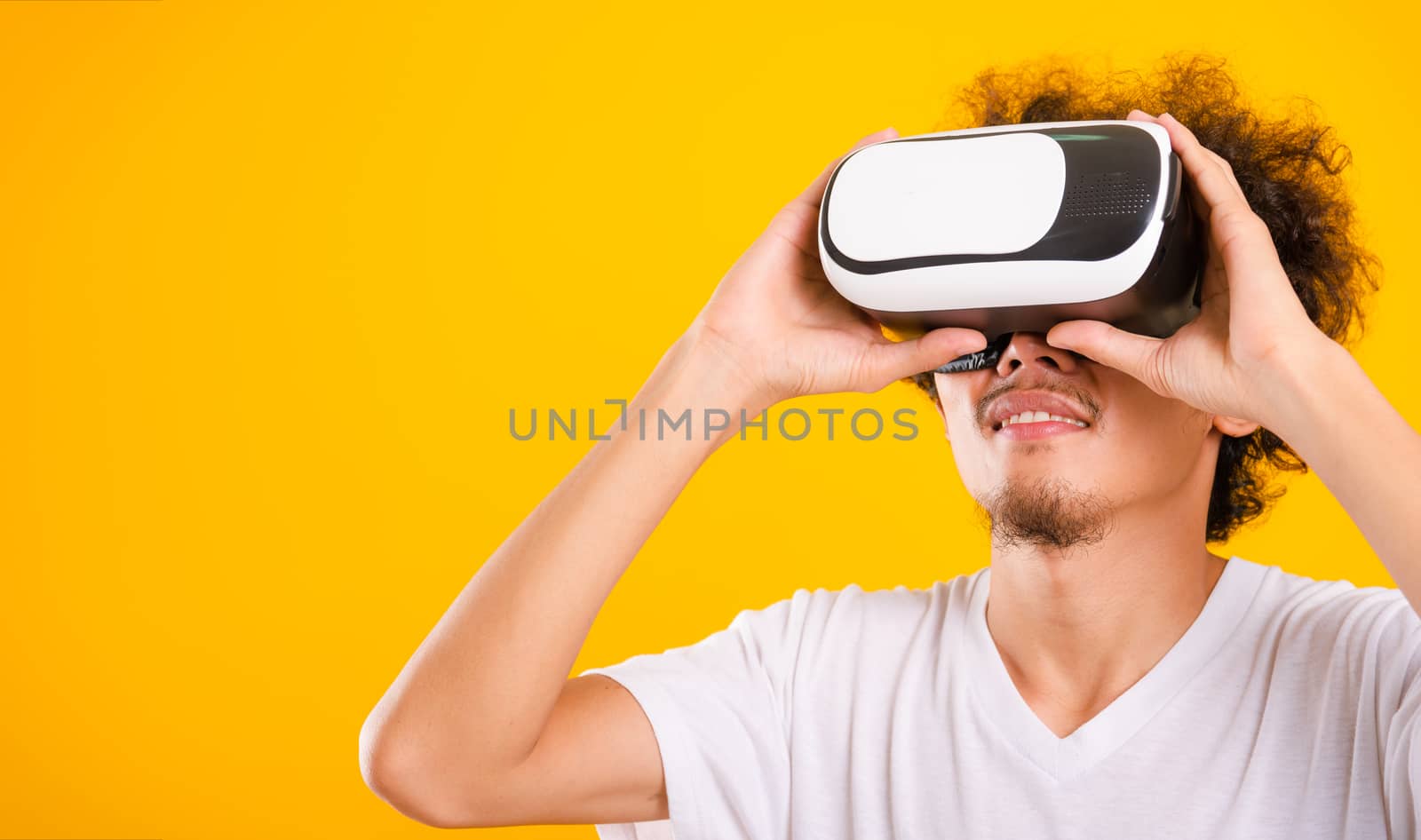 Asian handsome man with curly hair he using virtual reality headset or VR glass isolate on yellow background