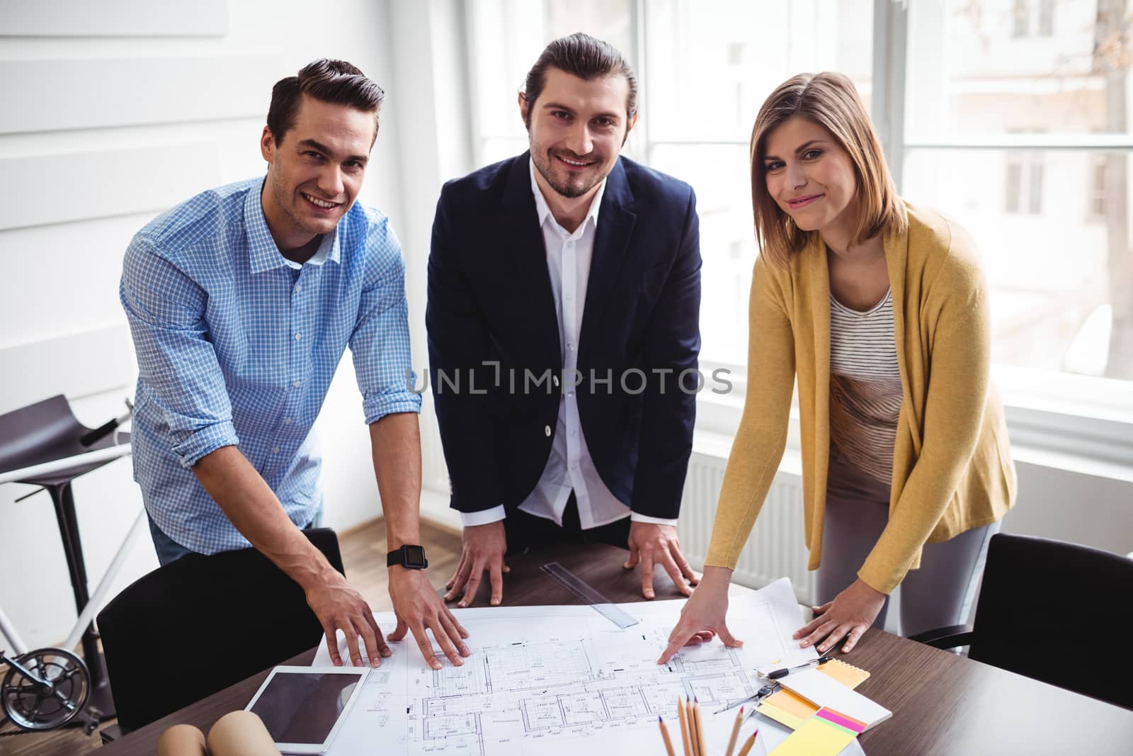 Portrait of smiling business people with blueprint at creative office