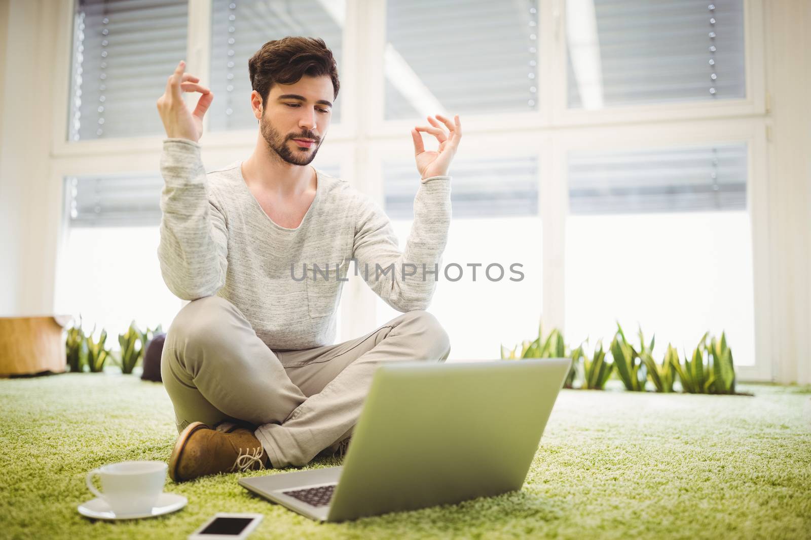 Young businessman doing yoga in front of laptop in creative office