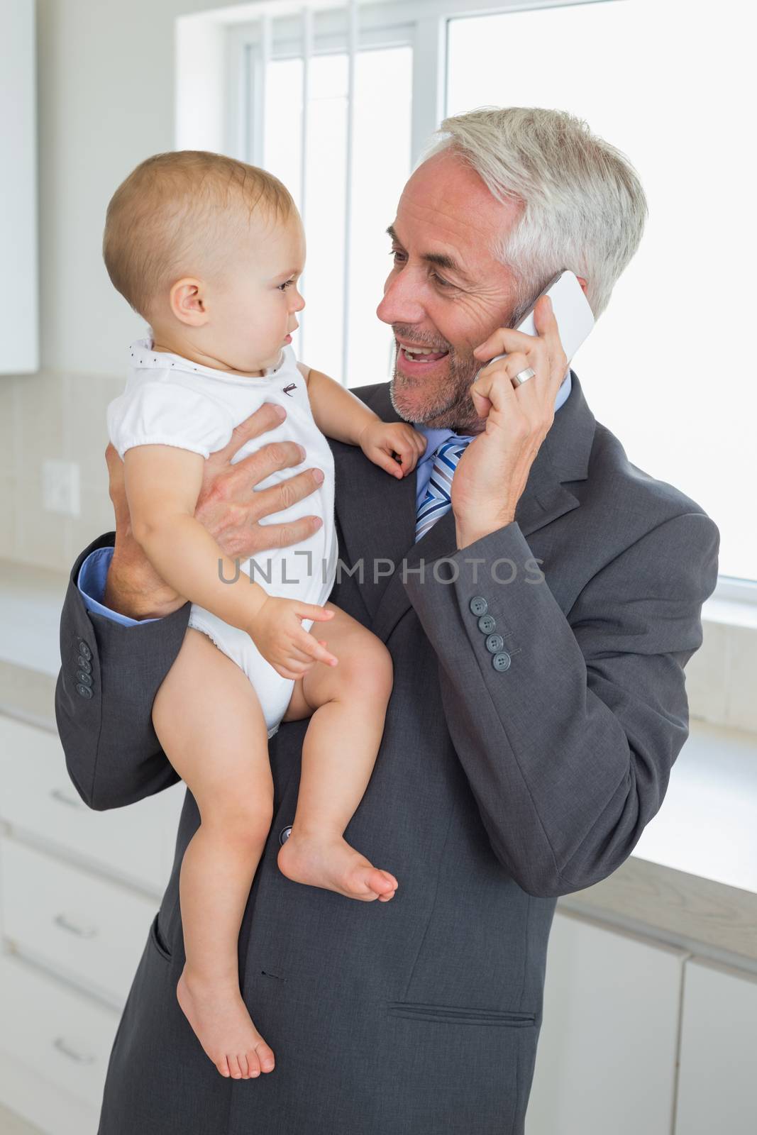 Smiling businessman holding his baby in the morning before work at home in the kitchen