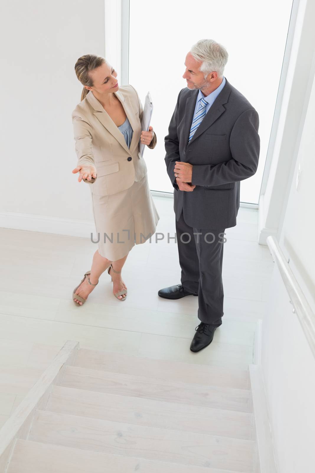 Smiling estate agent showing stairs to potential buyer by Wavebreakmedia