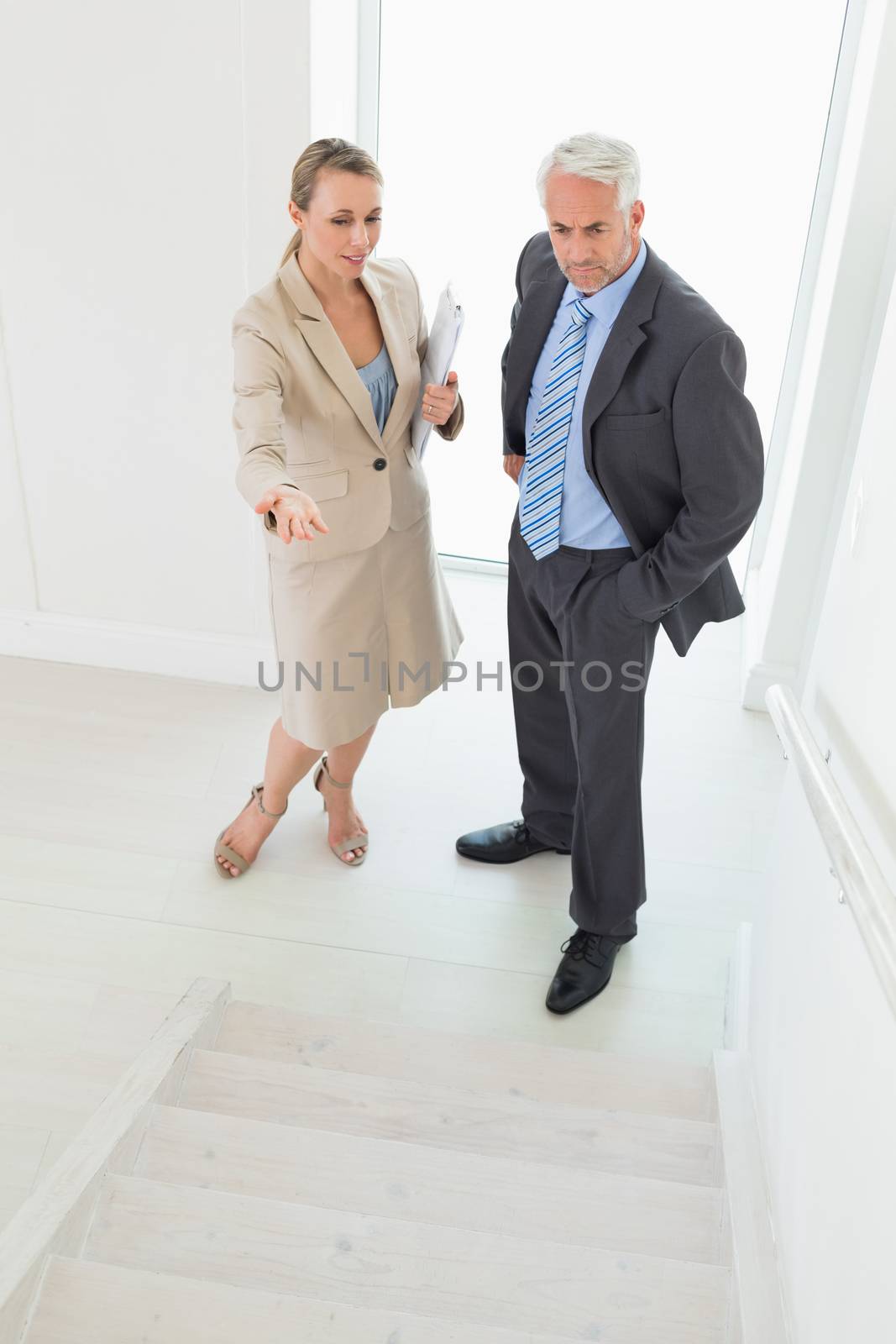 Smiling estate agent showing stairs to potential buyer in empty house