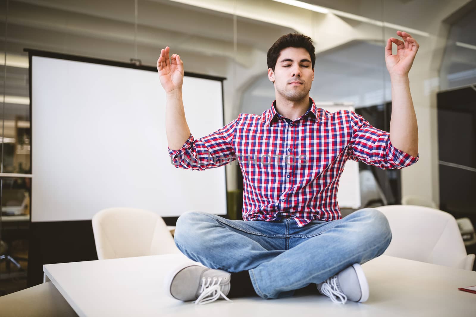 Full length of businessman performing yoga in meeting room at creative office