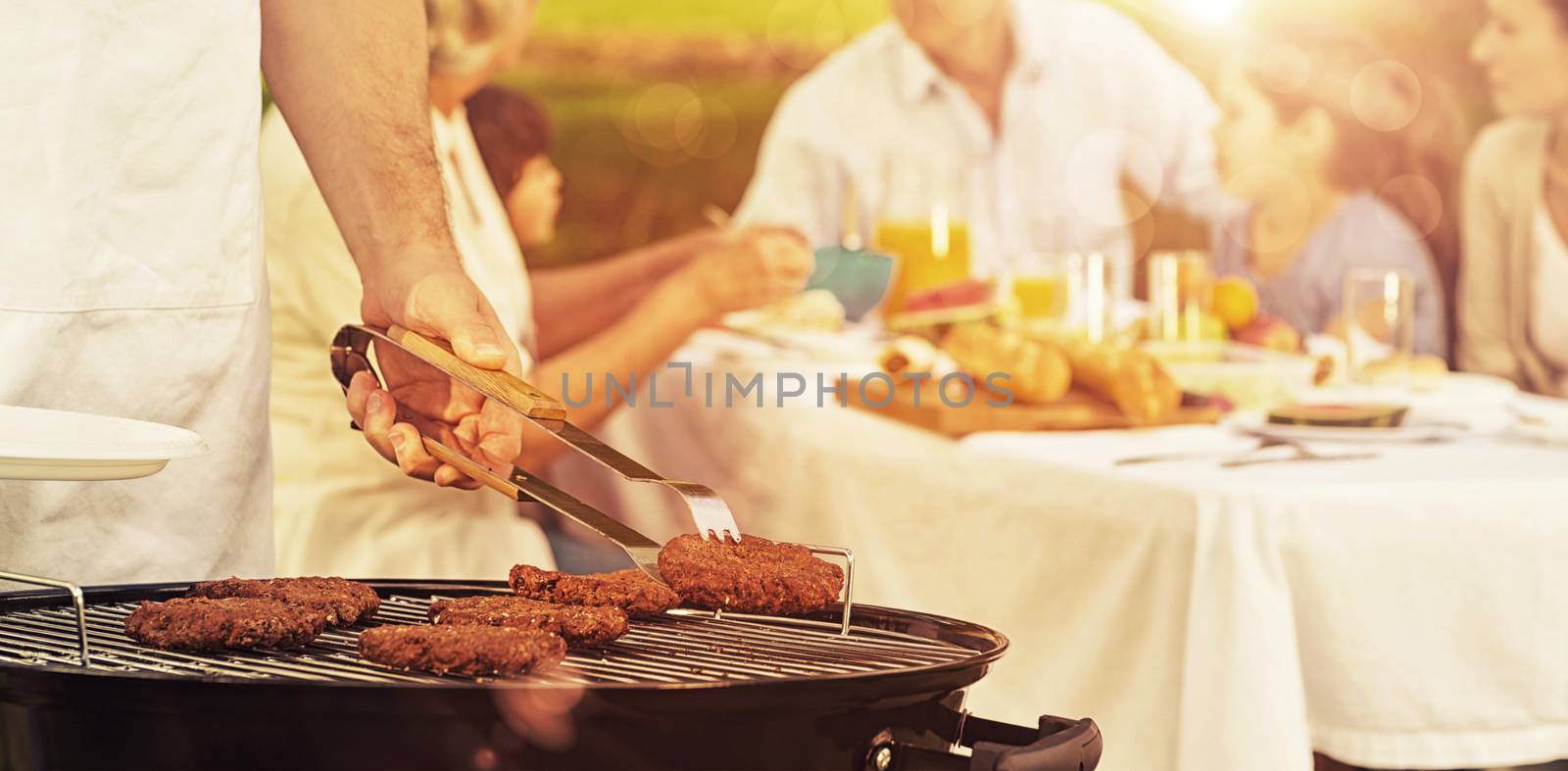 Close-up of barbecue grill with extended family having lunch in the park