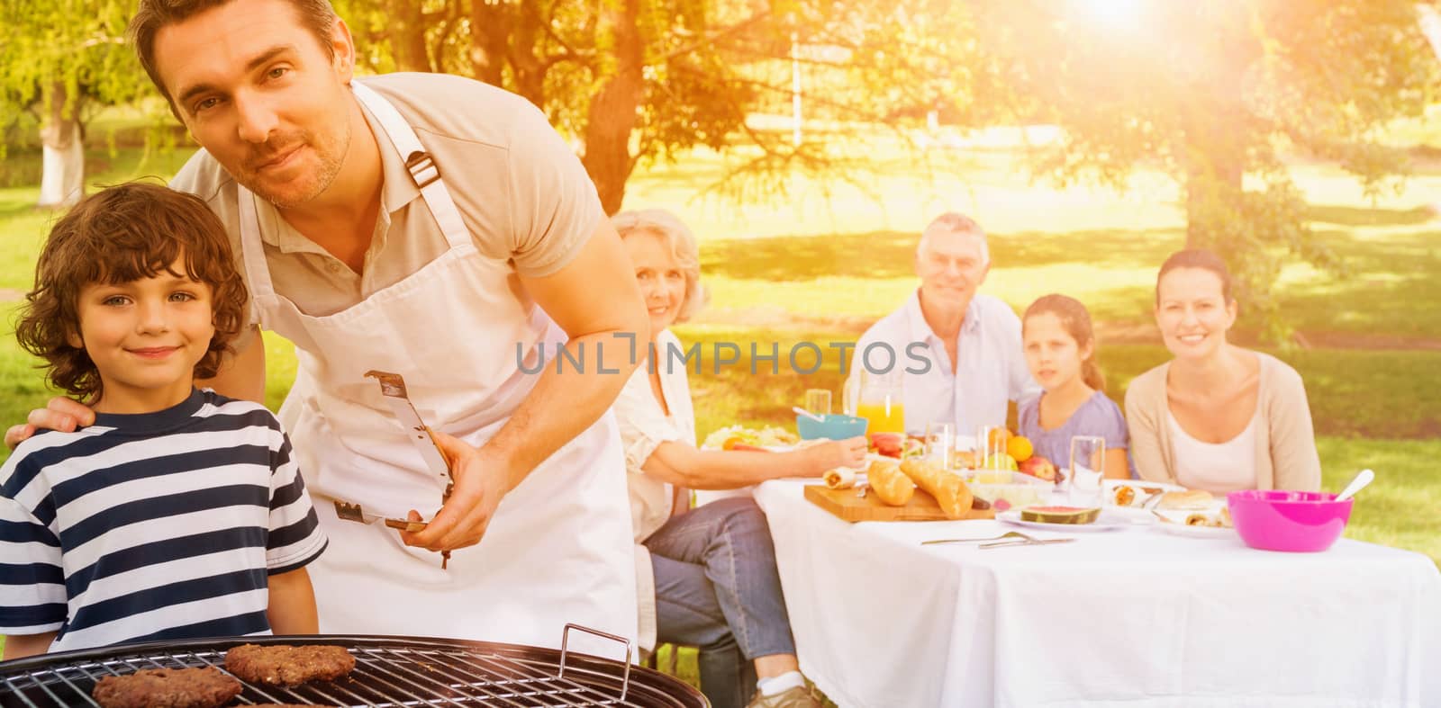 Father and son at barbecue grill with extended family having lunch in the park