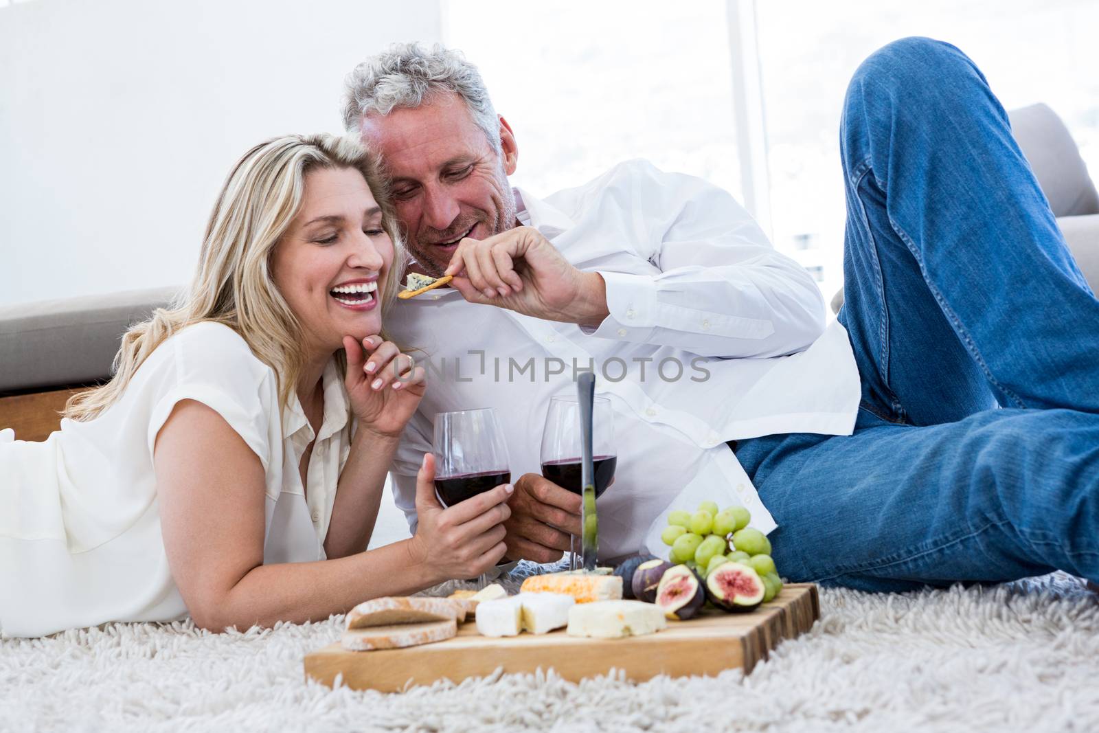 Romantic man feeding woman while lying on rug at home