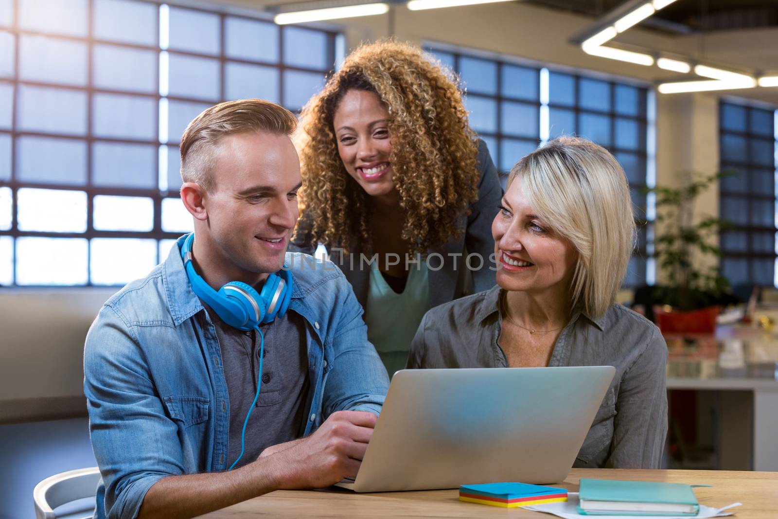 Happy creative business people discussing over laptop at desk in office