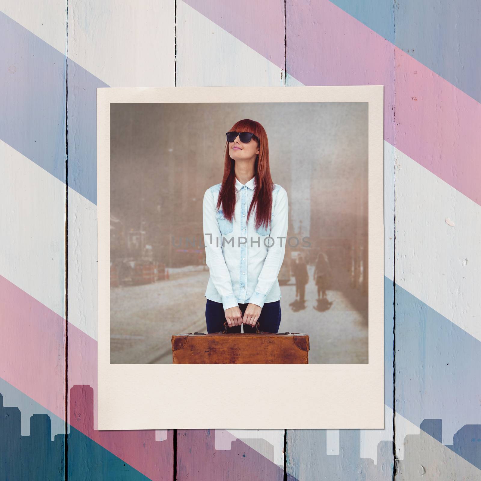 Smiling hipster woman holding suitcase against colored background