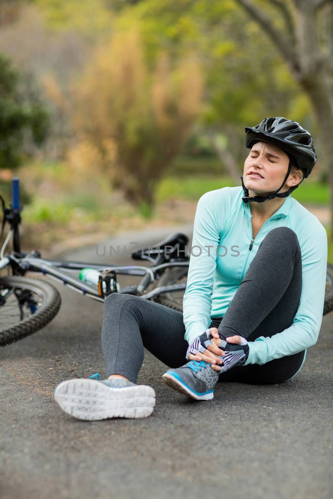 Female cyclist in pain holding her injured leg by Wavebreakmedia