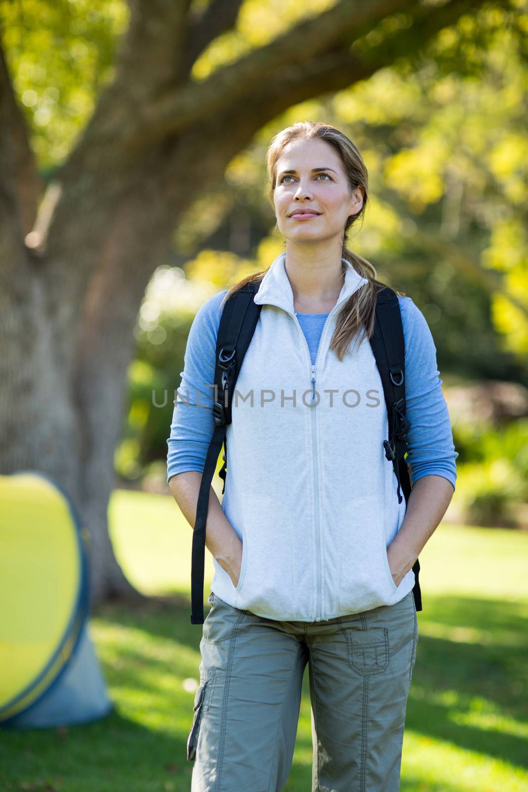 Thoughtful female hiker standing with hands in pockets in forest