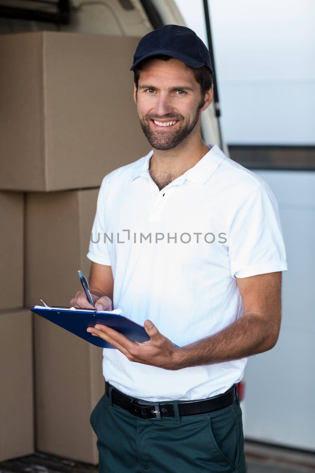 Delivery man writing on clipboard while standing next to his van by Wavebreakmedia