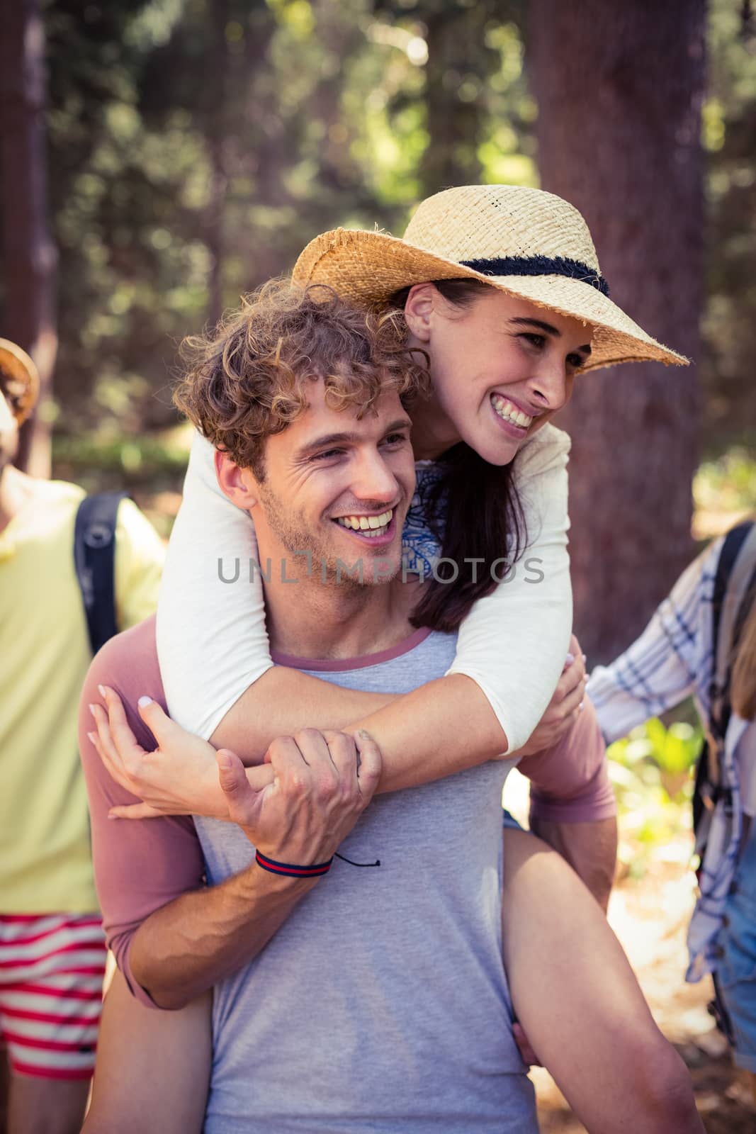 Man giving a piggyback ride to woman in forest on a sunny day
