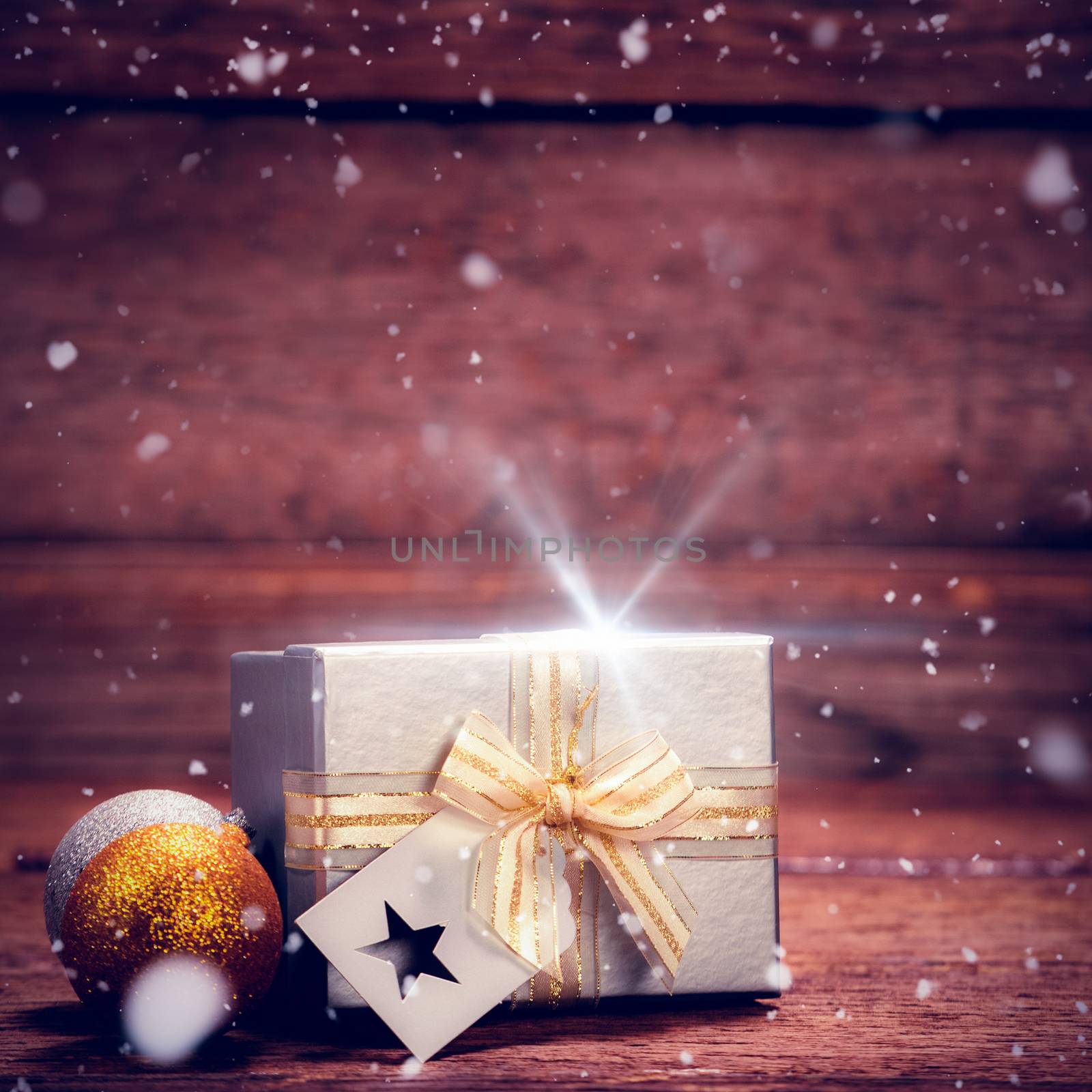 Snow falling against wrapped gift box and baubles on table