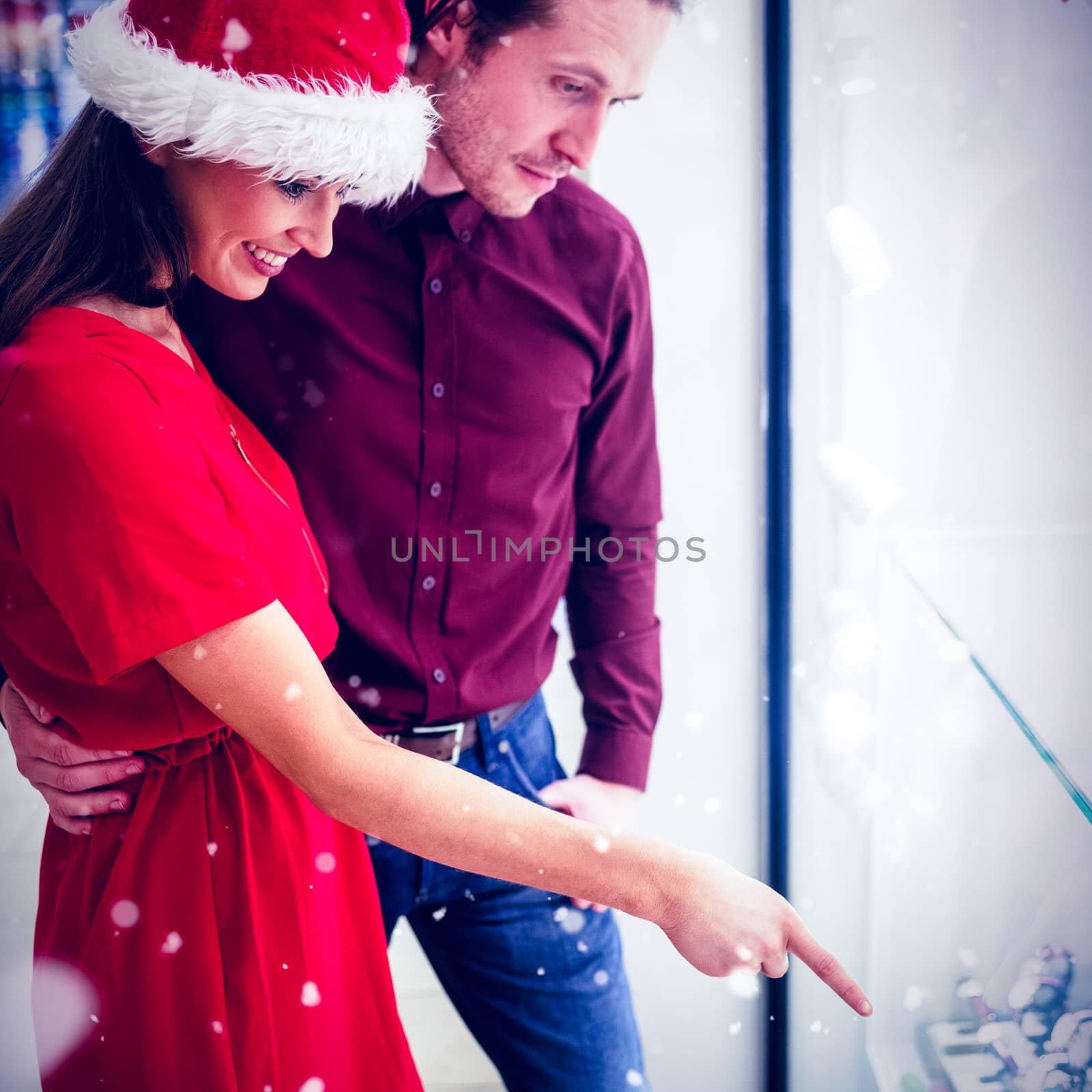 Side view of couple in Christmas attire looking at wrist watch display against snow falling