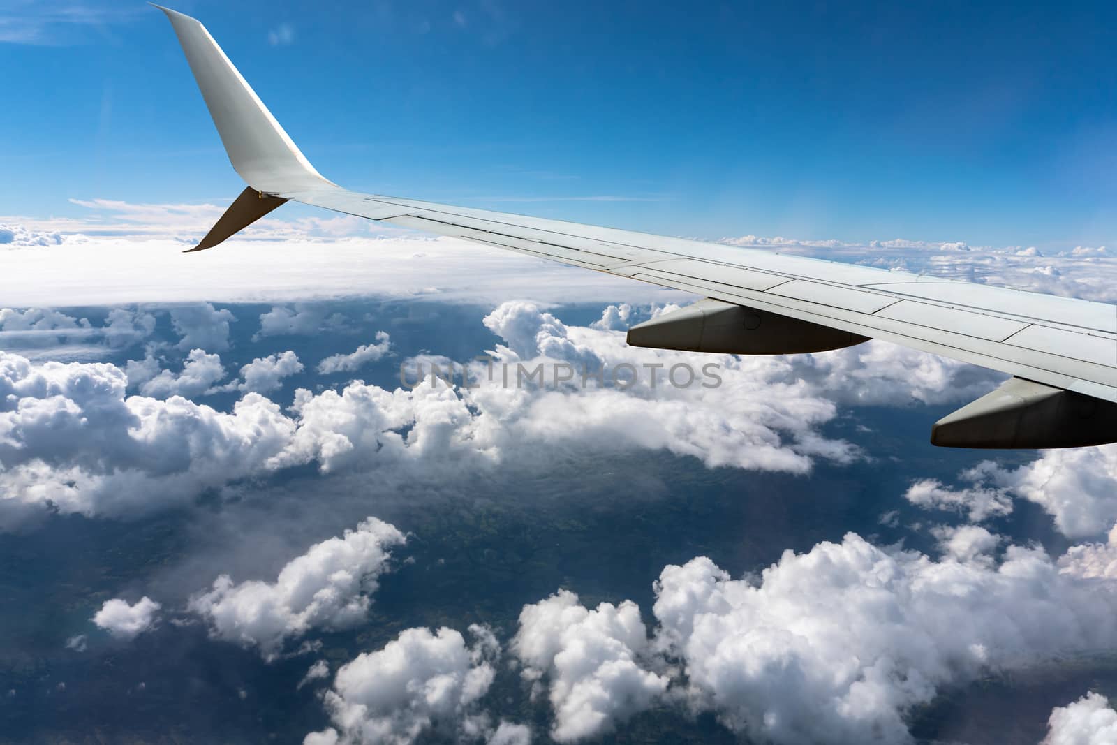 White clouds float under the wing of a sunlit airplane flying under a blue sky

