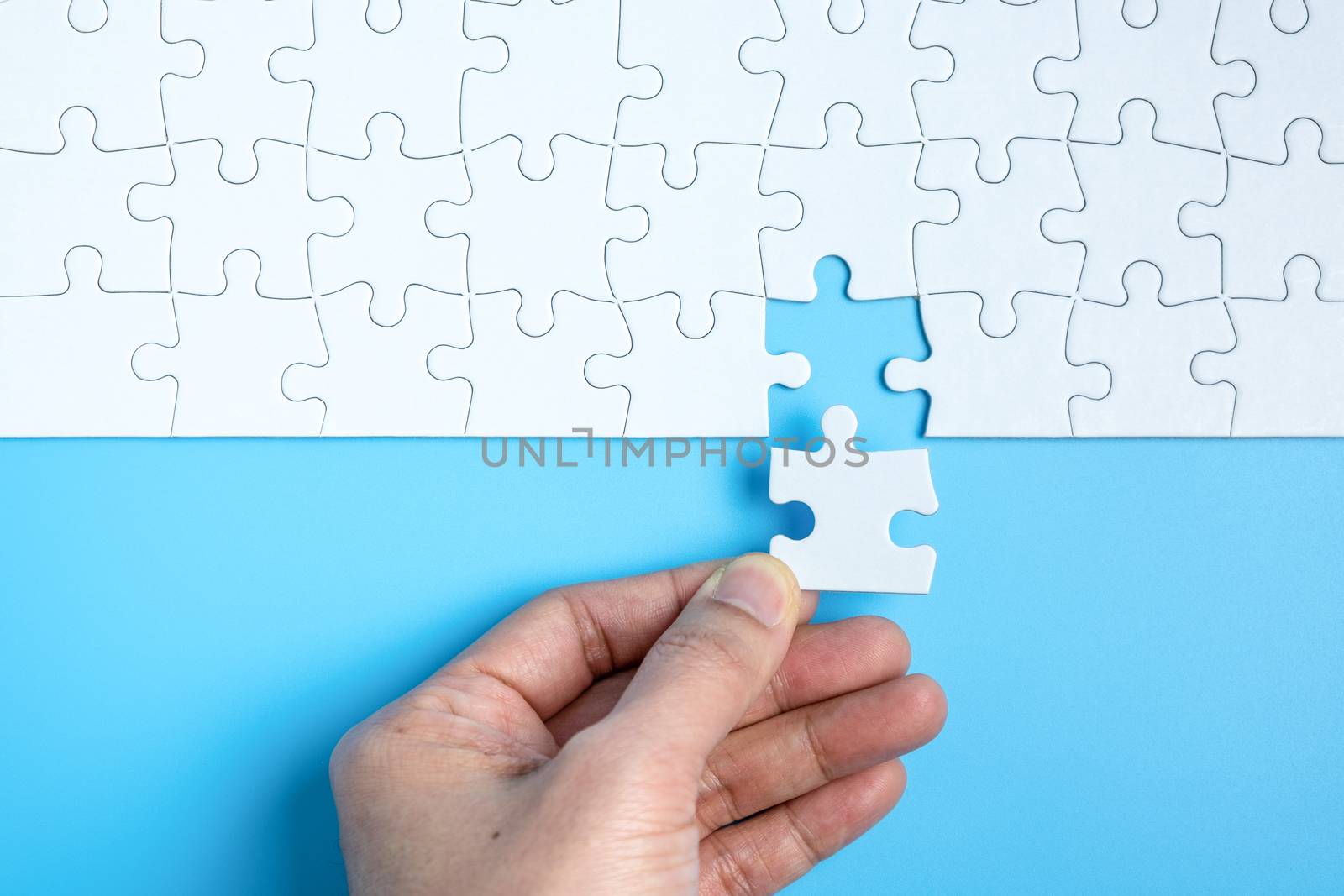 Hand putting the last piece of white jigsaw puzzle on blue background and place for your content
