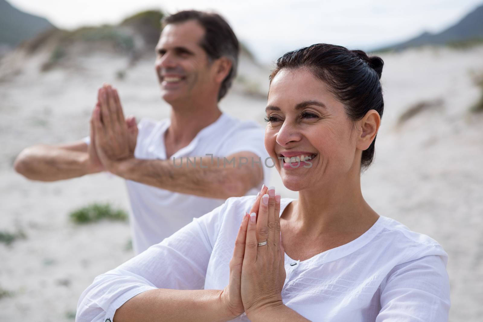 Couple performing yoga on beach by Wavebreakmedia