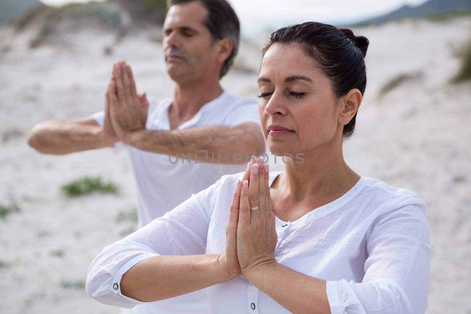 Couple performing yoga on beach during winter