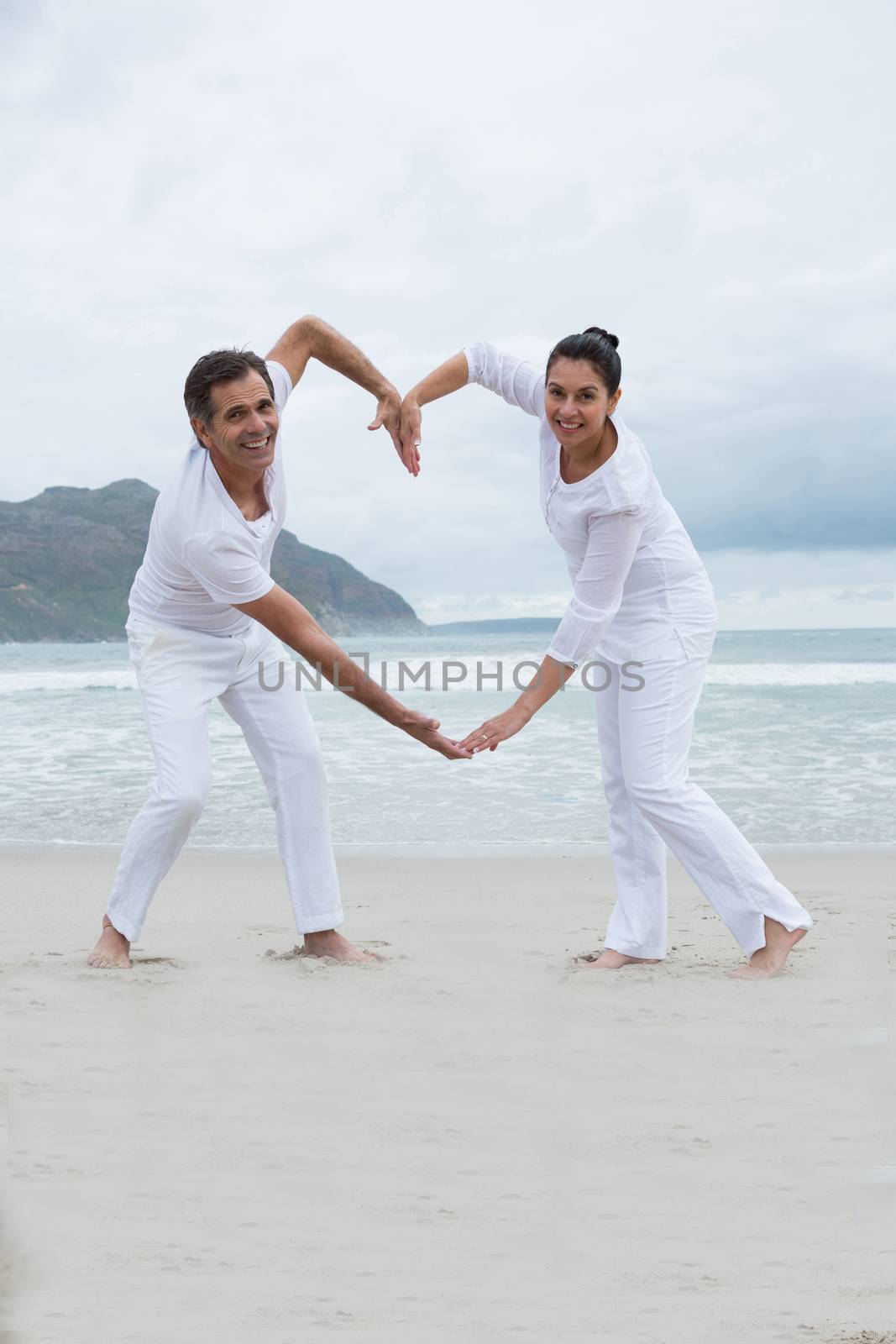 Romantic couple making heart by hands on beach by Wavebreakmedia