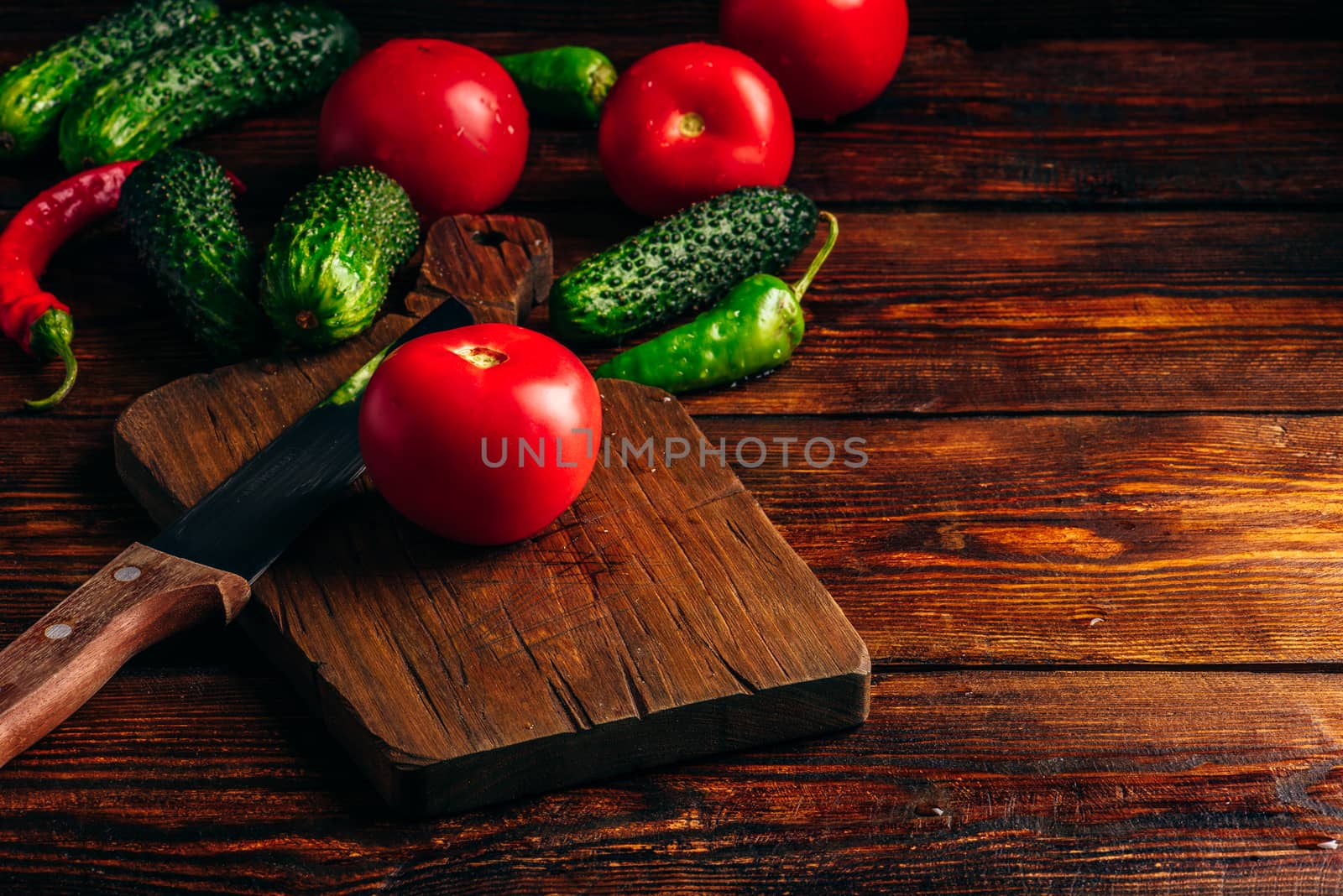 Fresh cucumbers, tomatoes and chili peppers on cutting board for preparing salad.