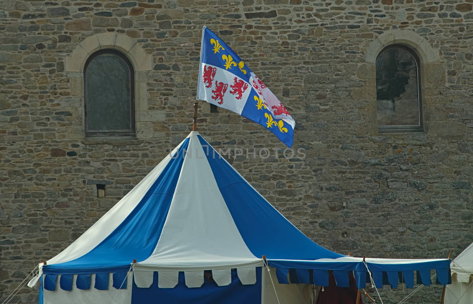Top of medieval blue and white tent with normandy flag at top and castle in background