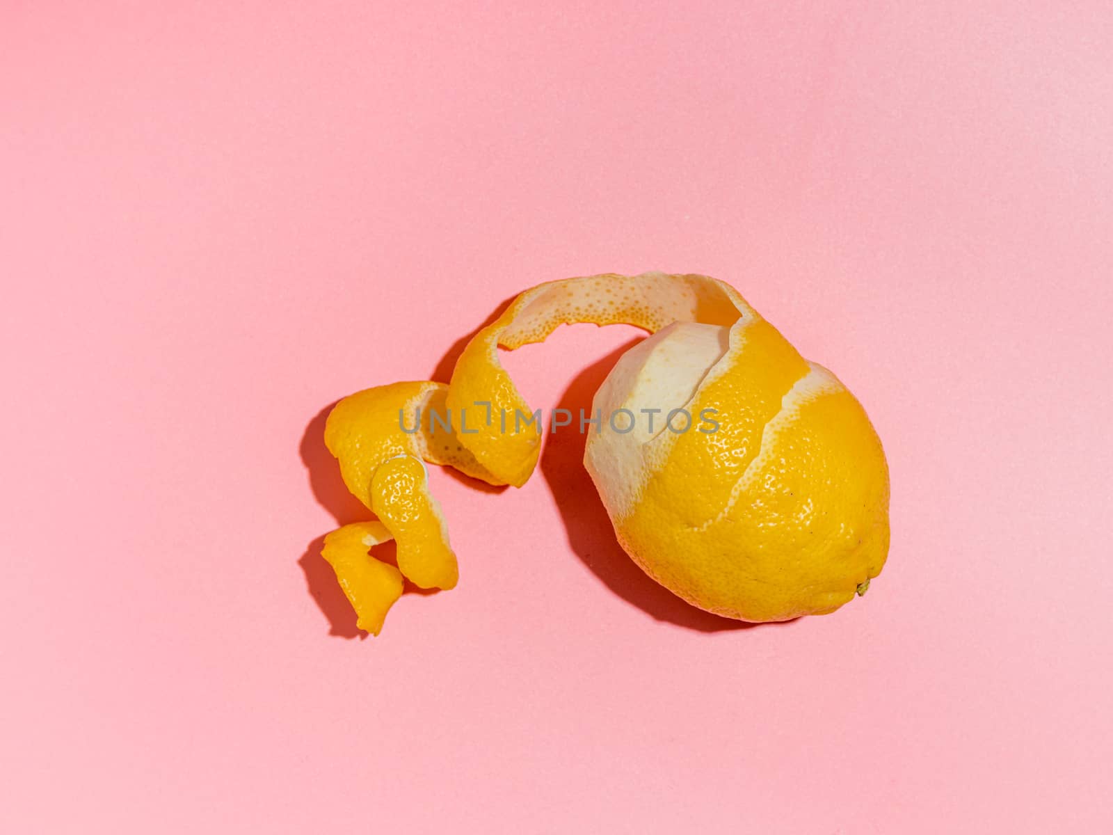 Lemon with spiral peeled zest over pink minimalistic background. Lemon and peel in hard light. Top view or flat lay. Summer minimalistic creative concept and layout