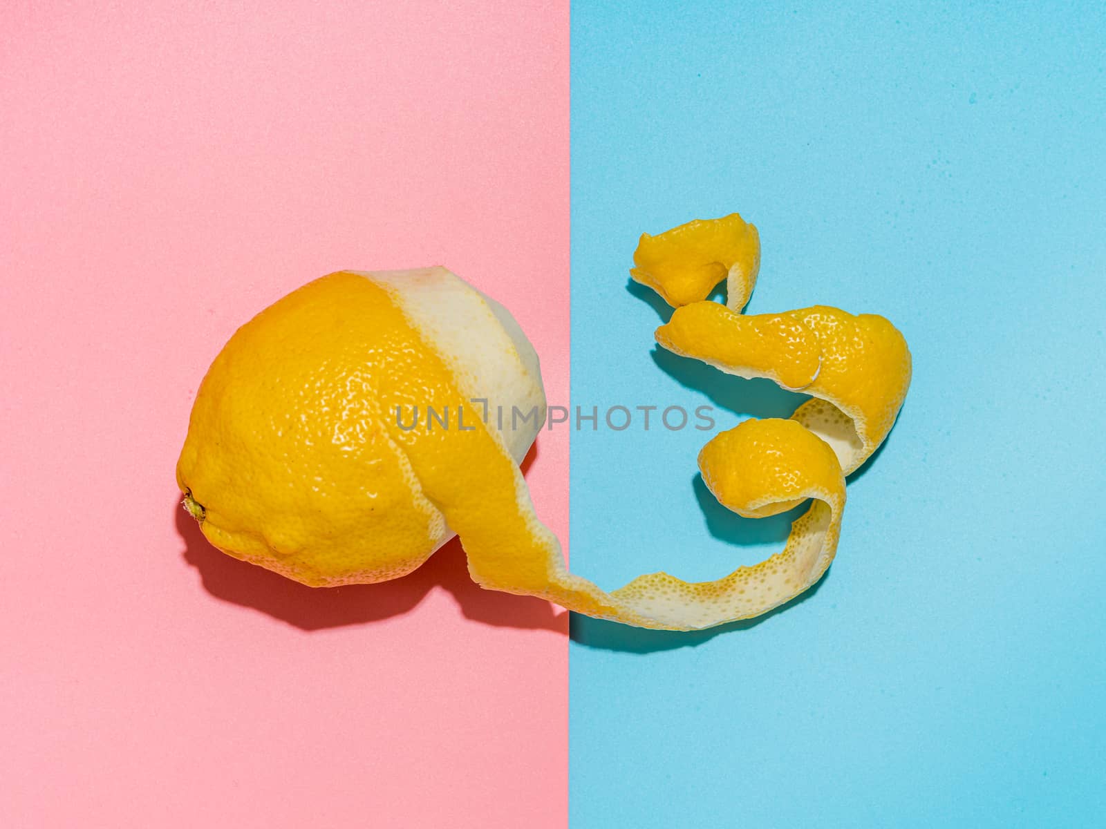 Lemon with spiral peeled zest over blue and pink minimalistic background. Lemon and peel in hard light. Top view or flat lay. Summer minimalistic creative concept and layout