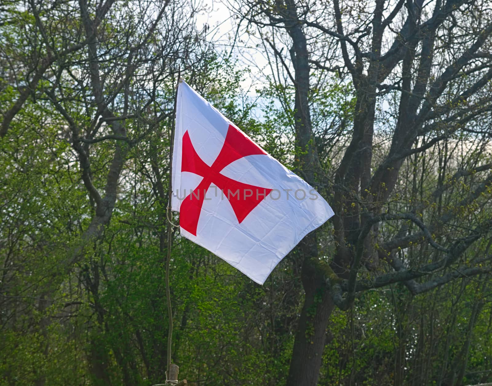 White flag with red cross flying on wind in front of an forest