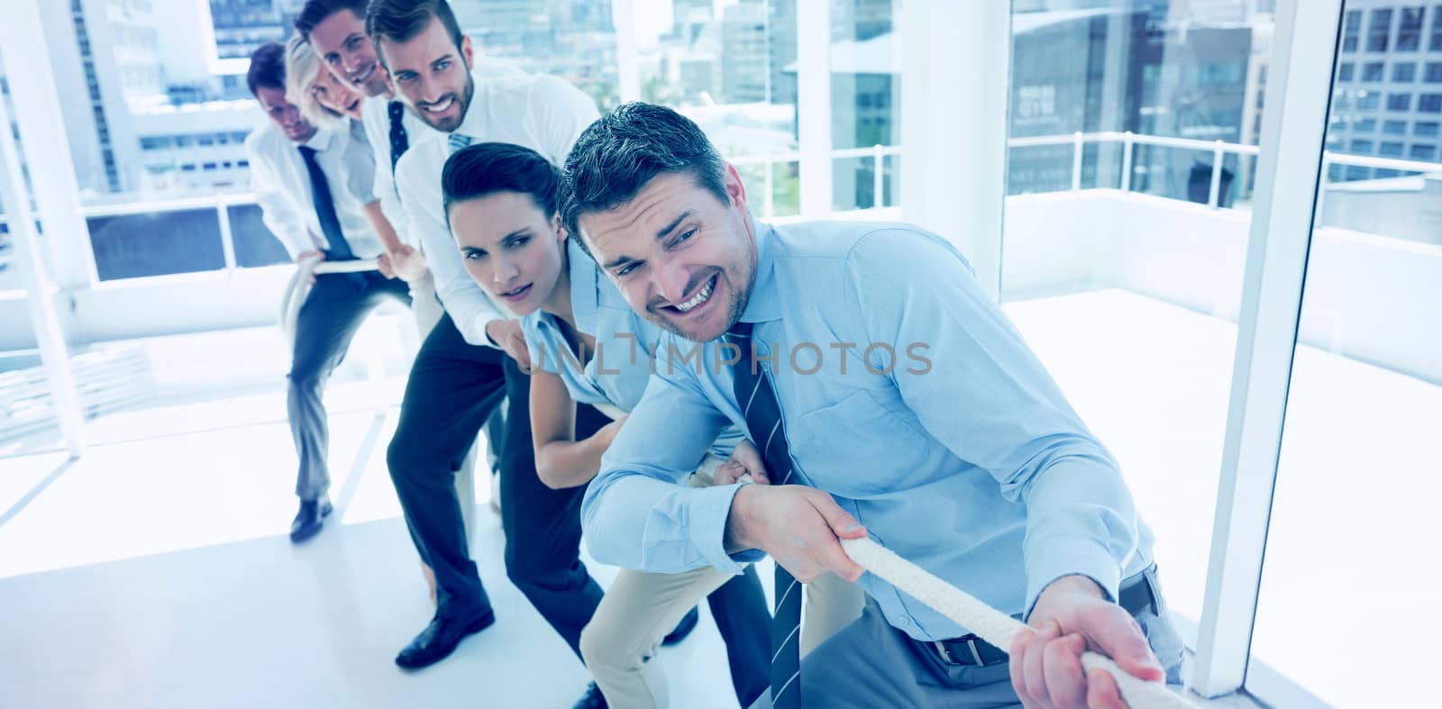 Full length of a group of business people pulling rope in a bright office