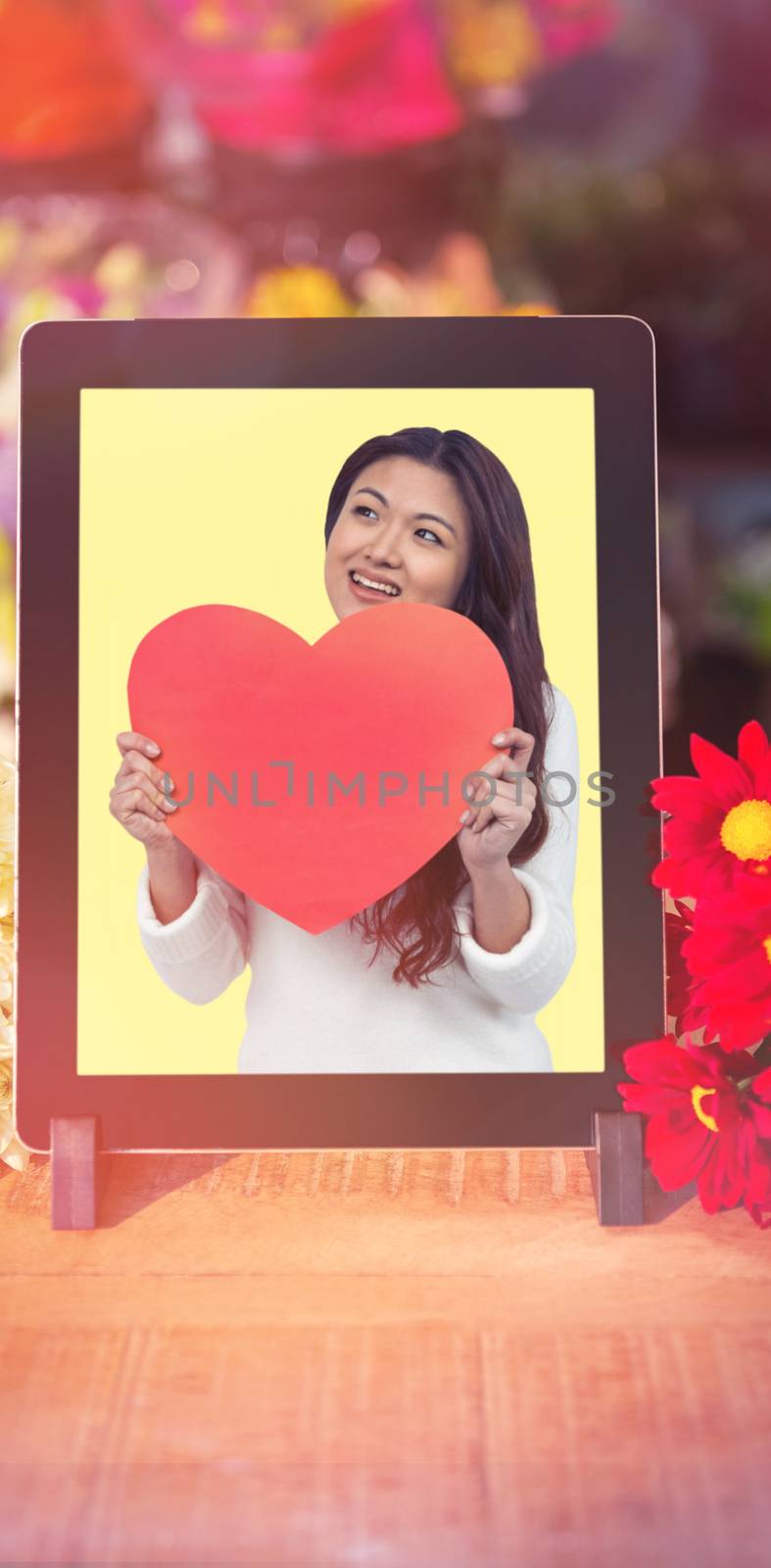 Smiling Asian woman holding paper heart against digital technology with flowers