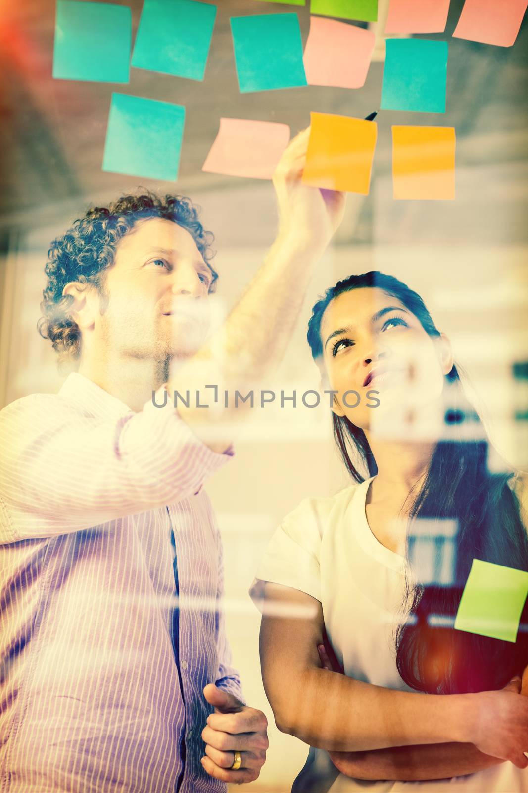 Businessman and businesswoman discussing over adhesive notes on glass wall in office