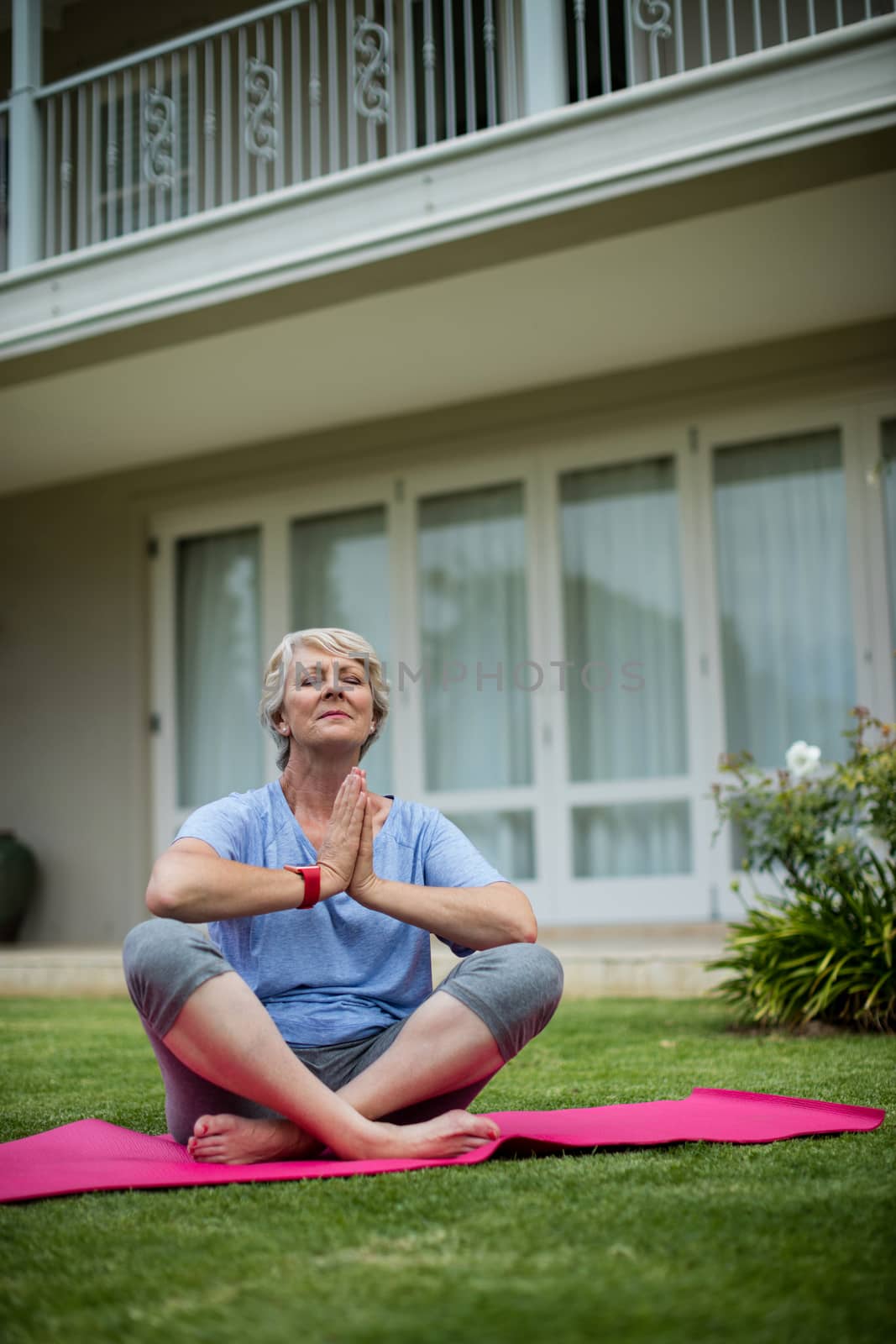 Senior woman practising yoga on exercise mat in lawn