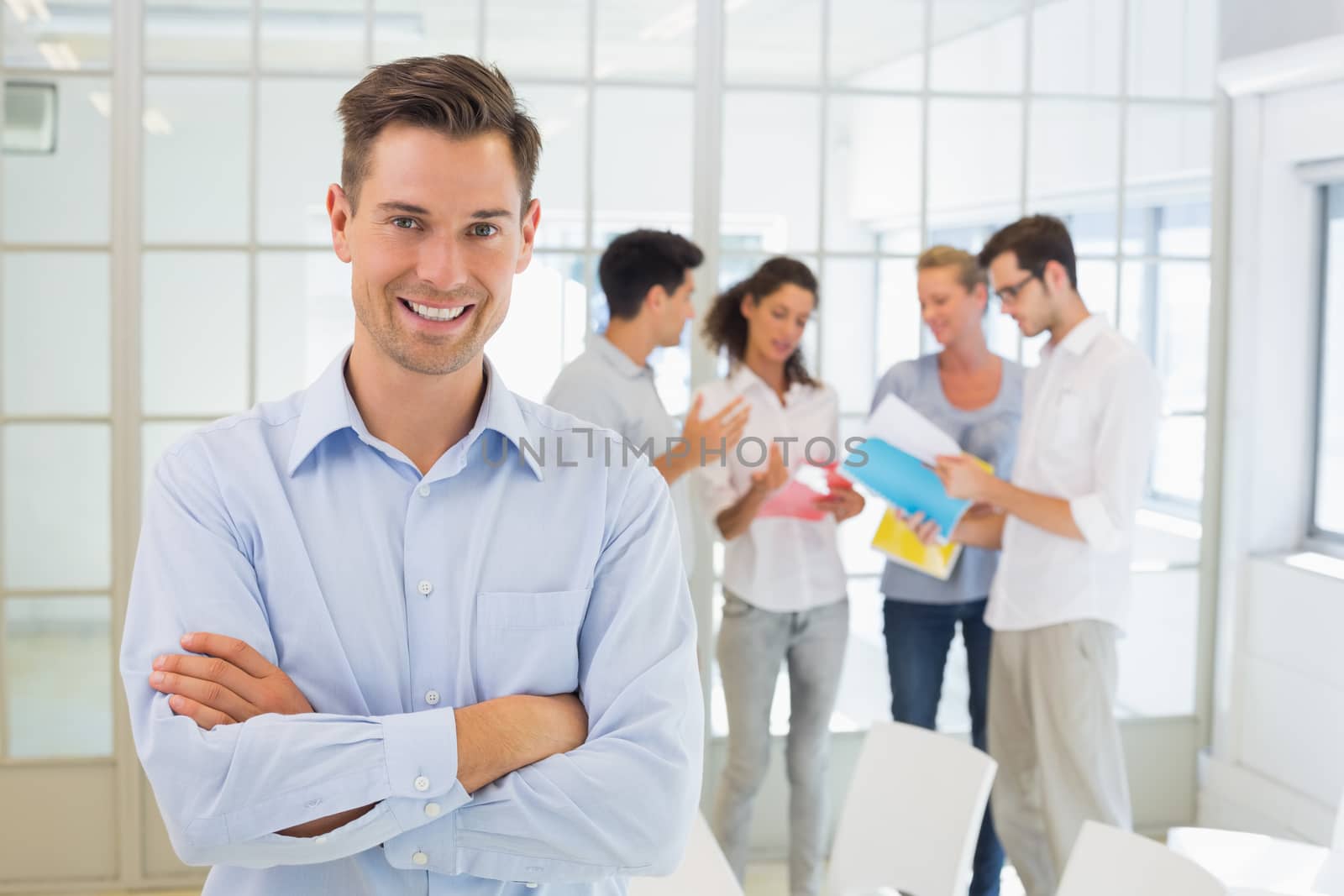Casual boss smiling at camera in front of his team in the office