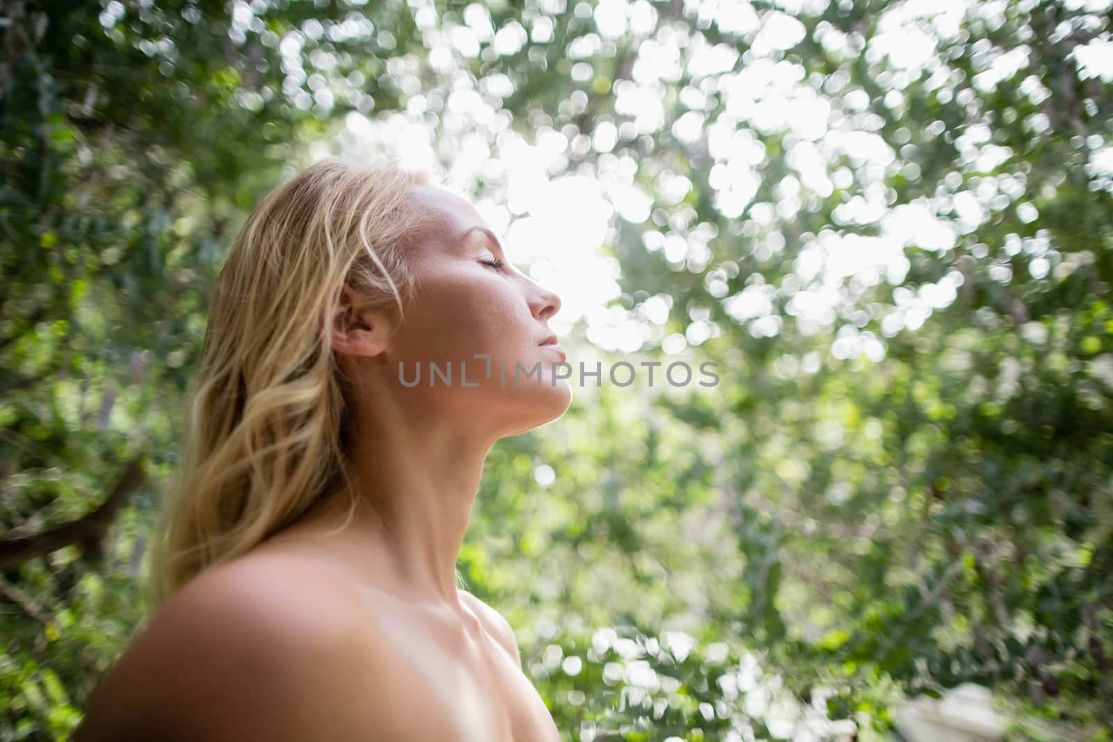 Beautiful woman meditating against bright sunlight in park