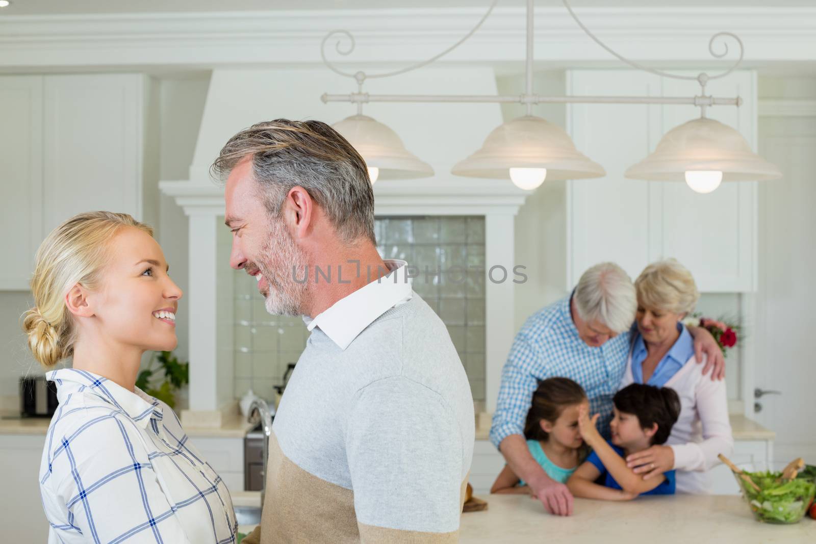 Romantic couple looking face to face at kitchen and family standing in background